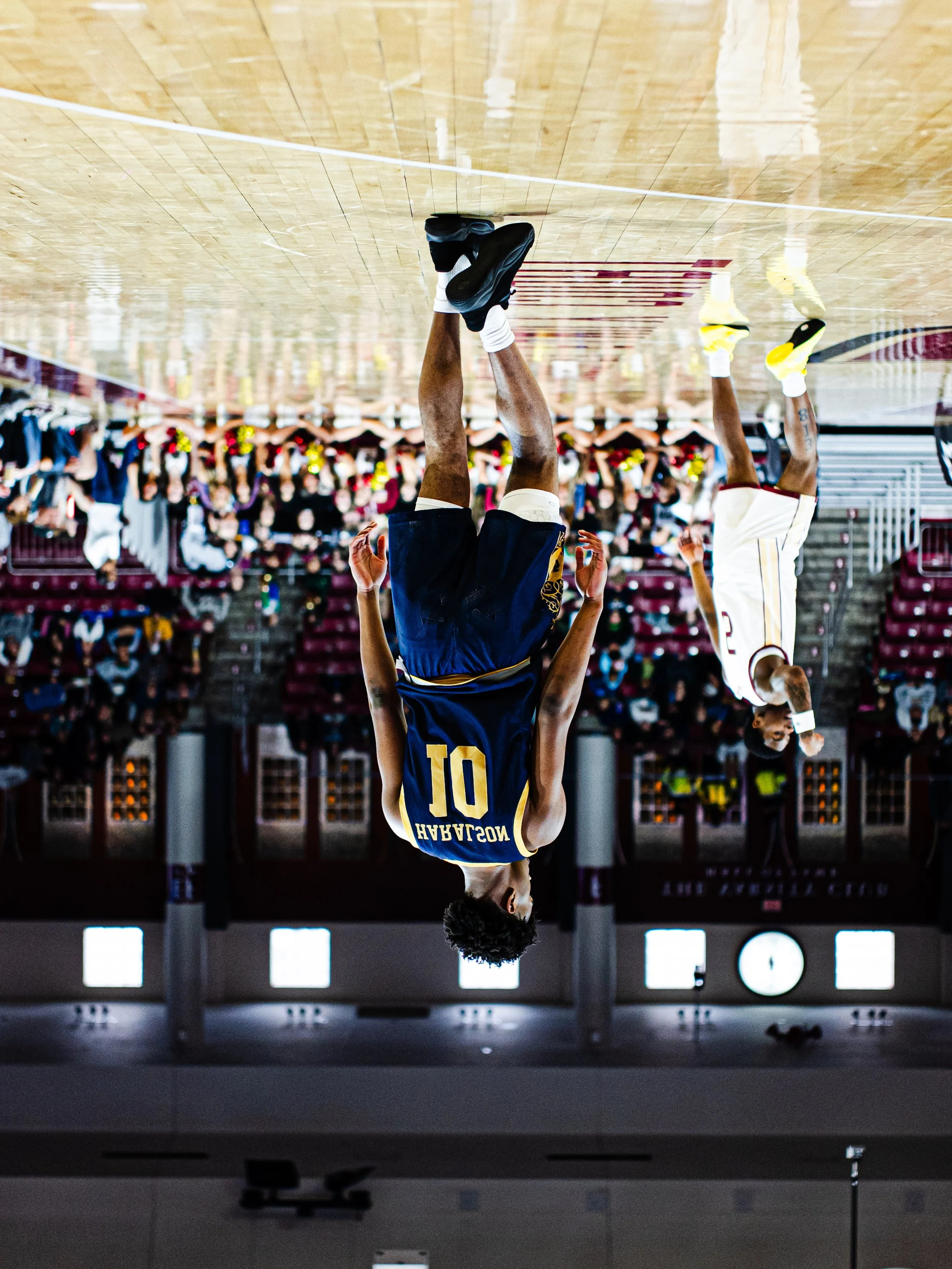 A basketball player wearing a blue jersey with the name 'NOSSALAH' and number 10, is jumping and aiming to make a shot during a game, with an audience in the background.