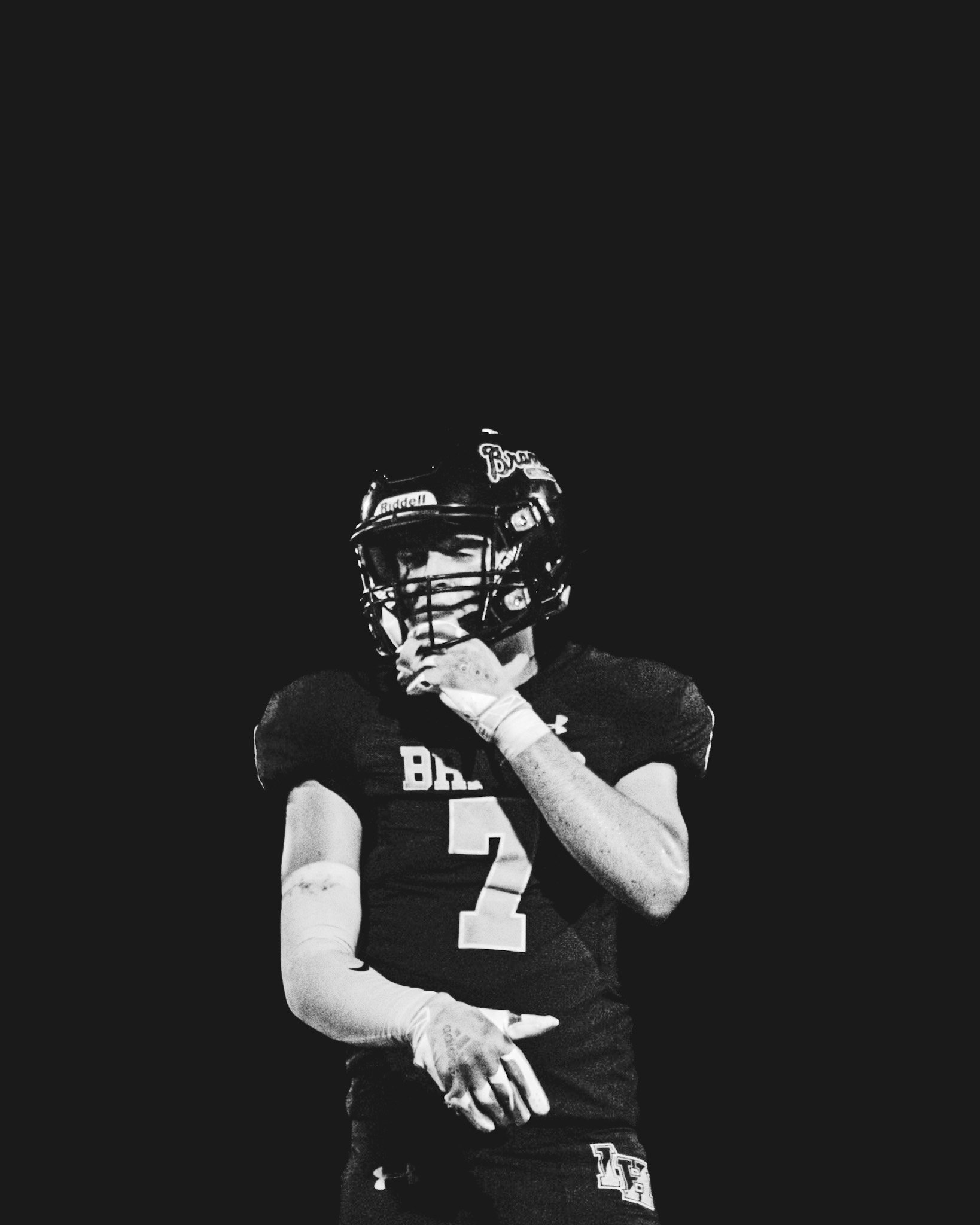 A football player in uniform with the number 2 on the chest and a helmet with a face guard, gloves, and athletic gear, against a dark background.