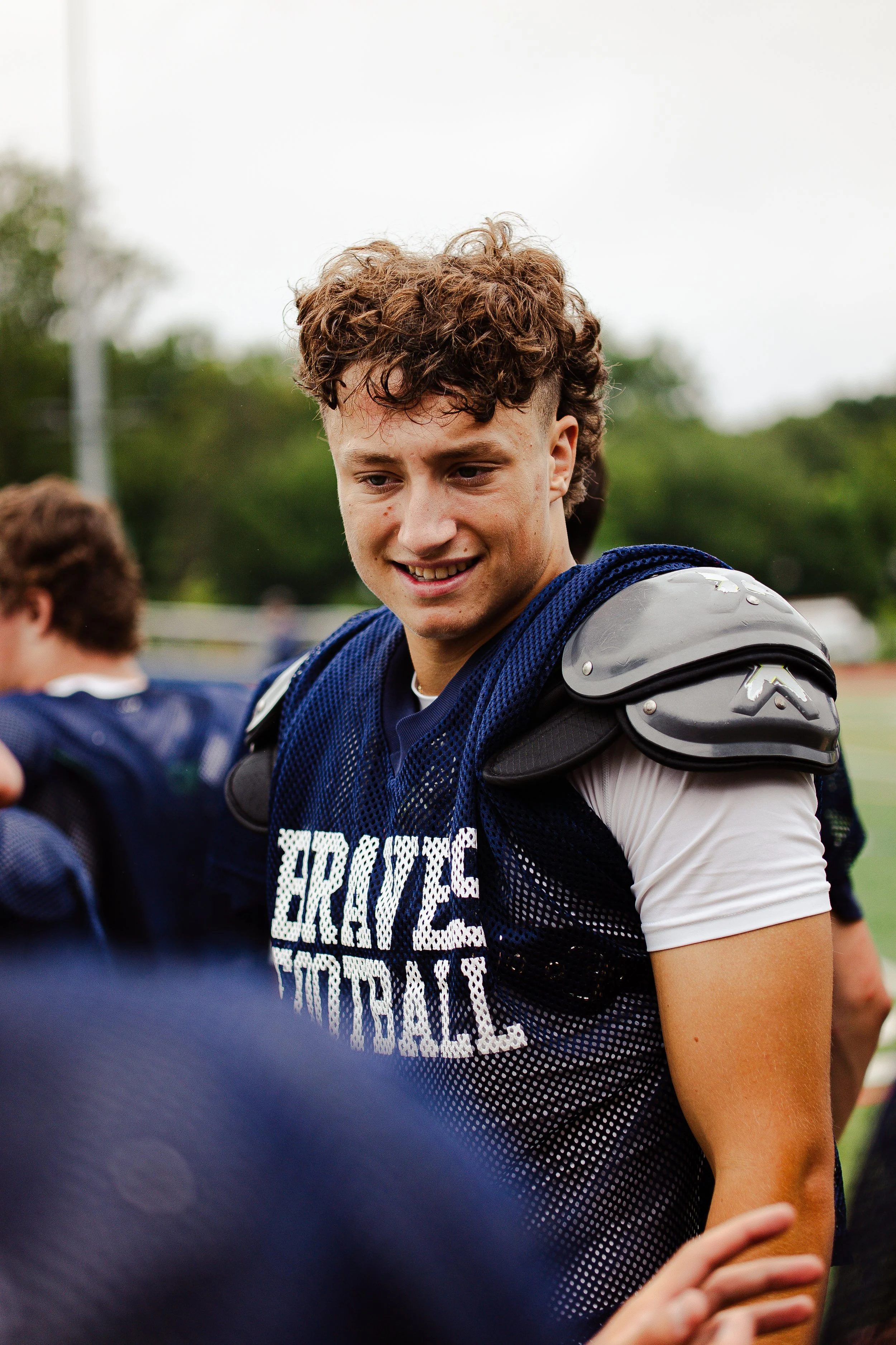 Young football player in uniform and shoulder pads smiling on the field.