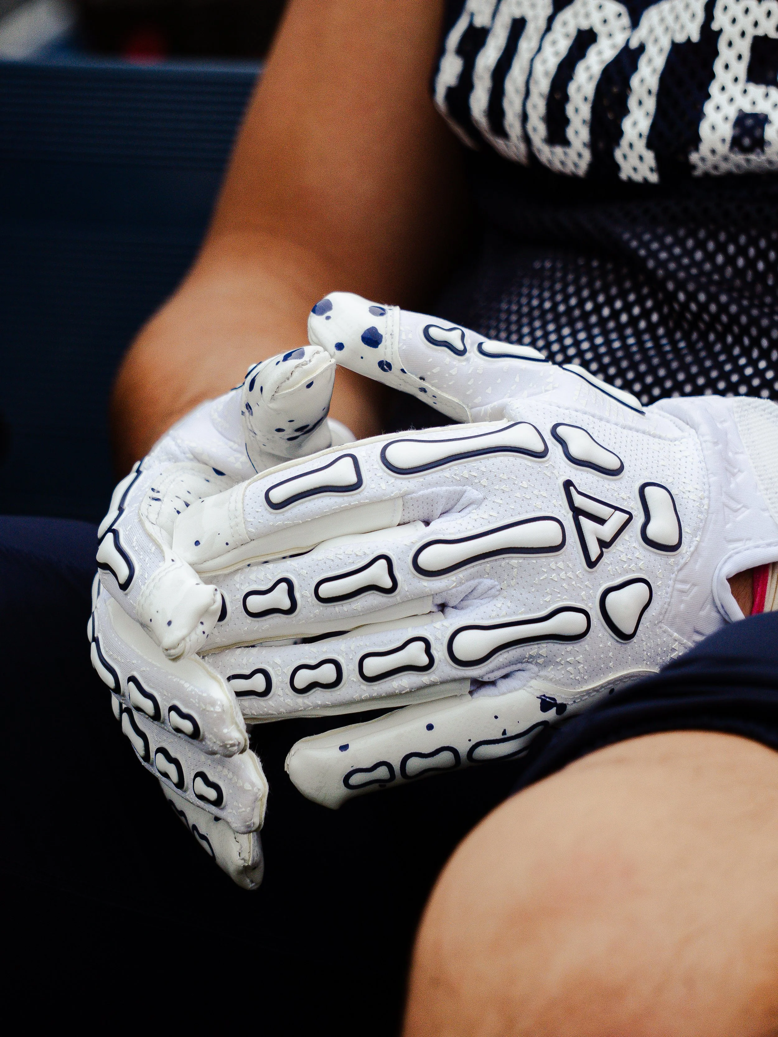 A person wearing a white and blue football or baseball glove, with a focus on the glove's fingers and surface, and part of the person's arm and clothing visible.