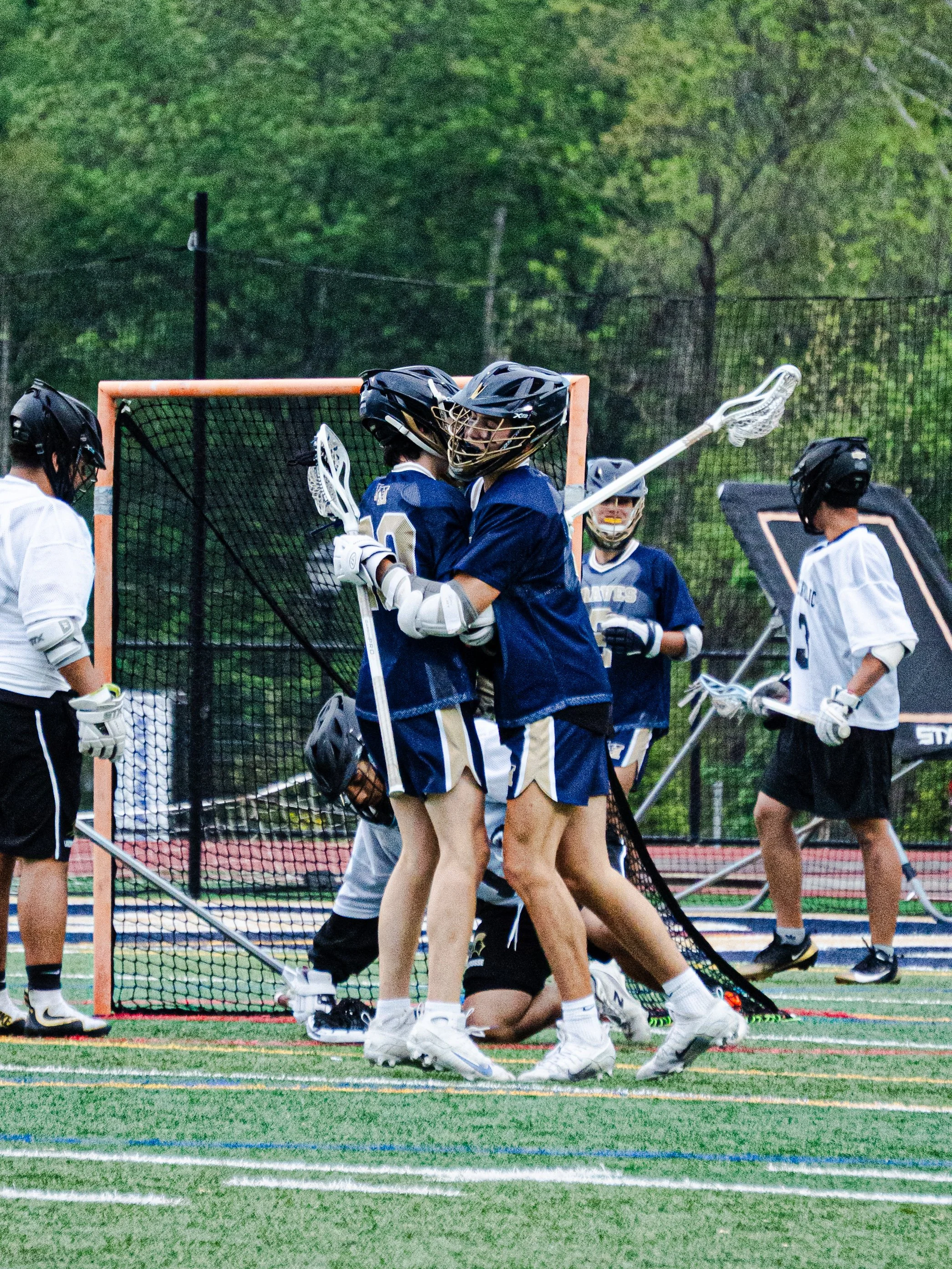 Lacrosse players gathered near the goal net on a sports field, celebrating or discussing during a game.