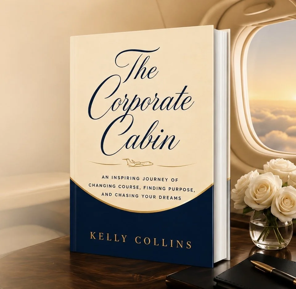 A book titled 'The Corporate Cabin' by Kelly Collins is standing on a wooden surface next to a vase of white roses. The background shows an airplane window with a sunset sky.
