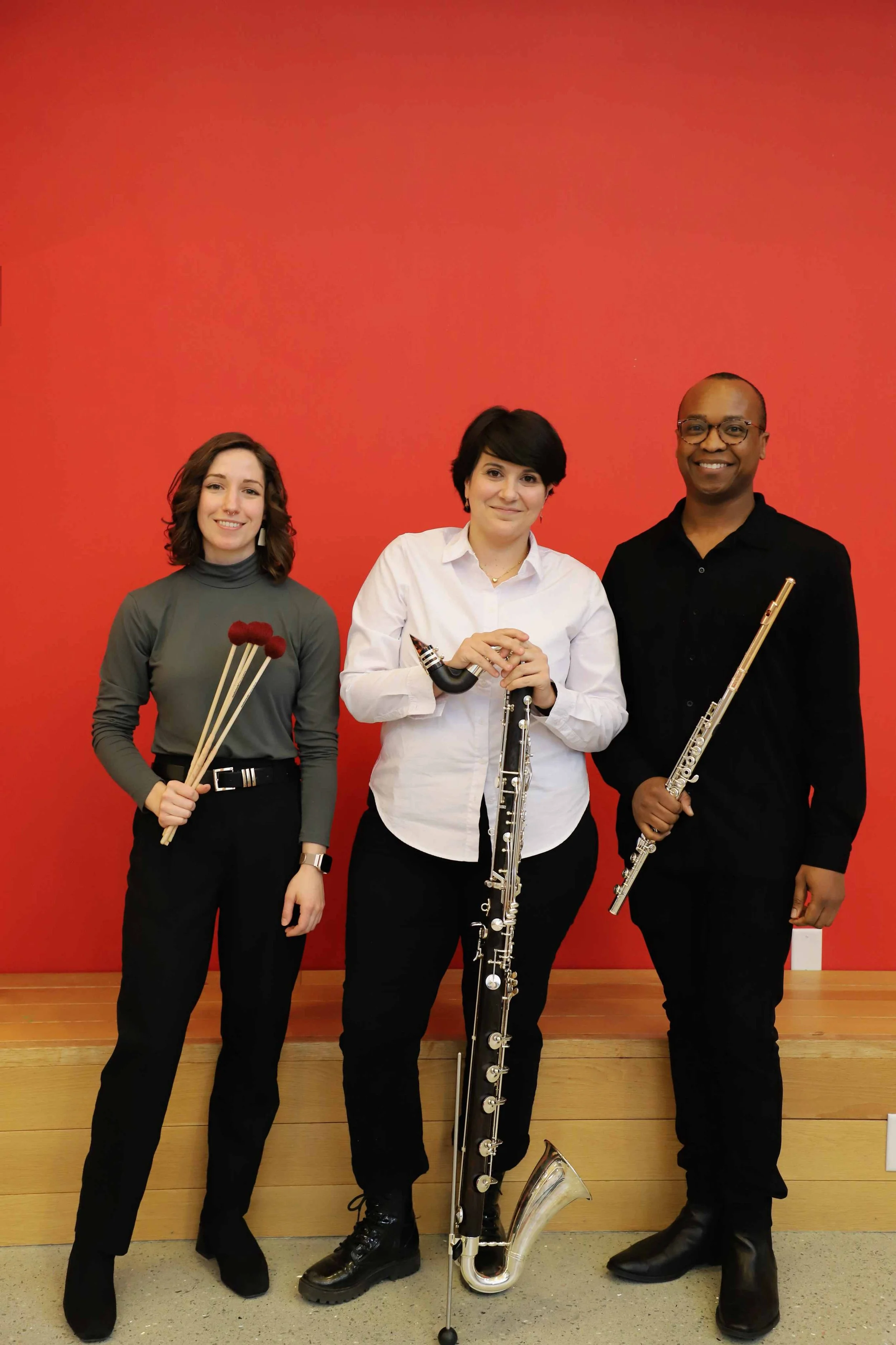 Three members of the Crane Faculty (Trio Con Brio) stand holding their instruments (percussion mallets, a bass clarinet, and flute).