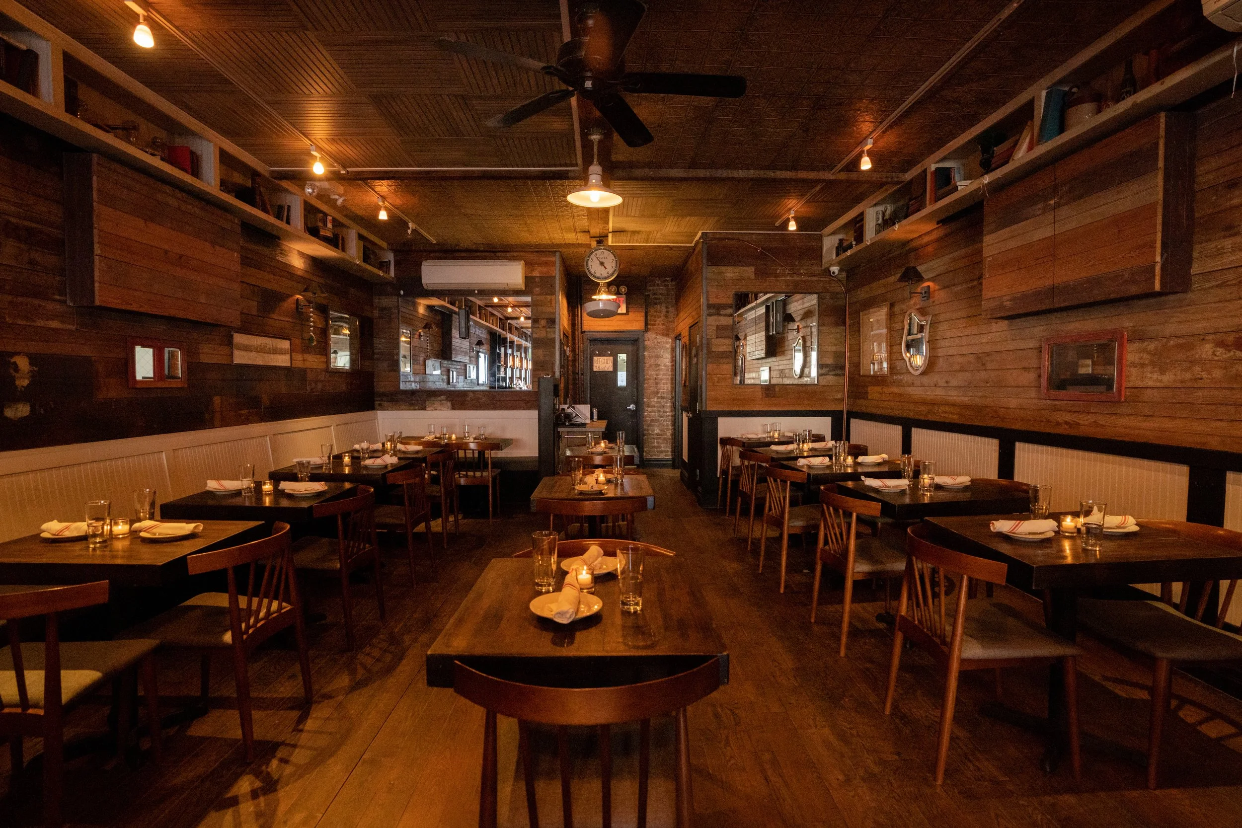 Interior of a cozy restaurant with wooden walls, tables set for dining, and warm lighting.