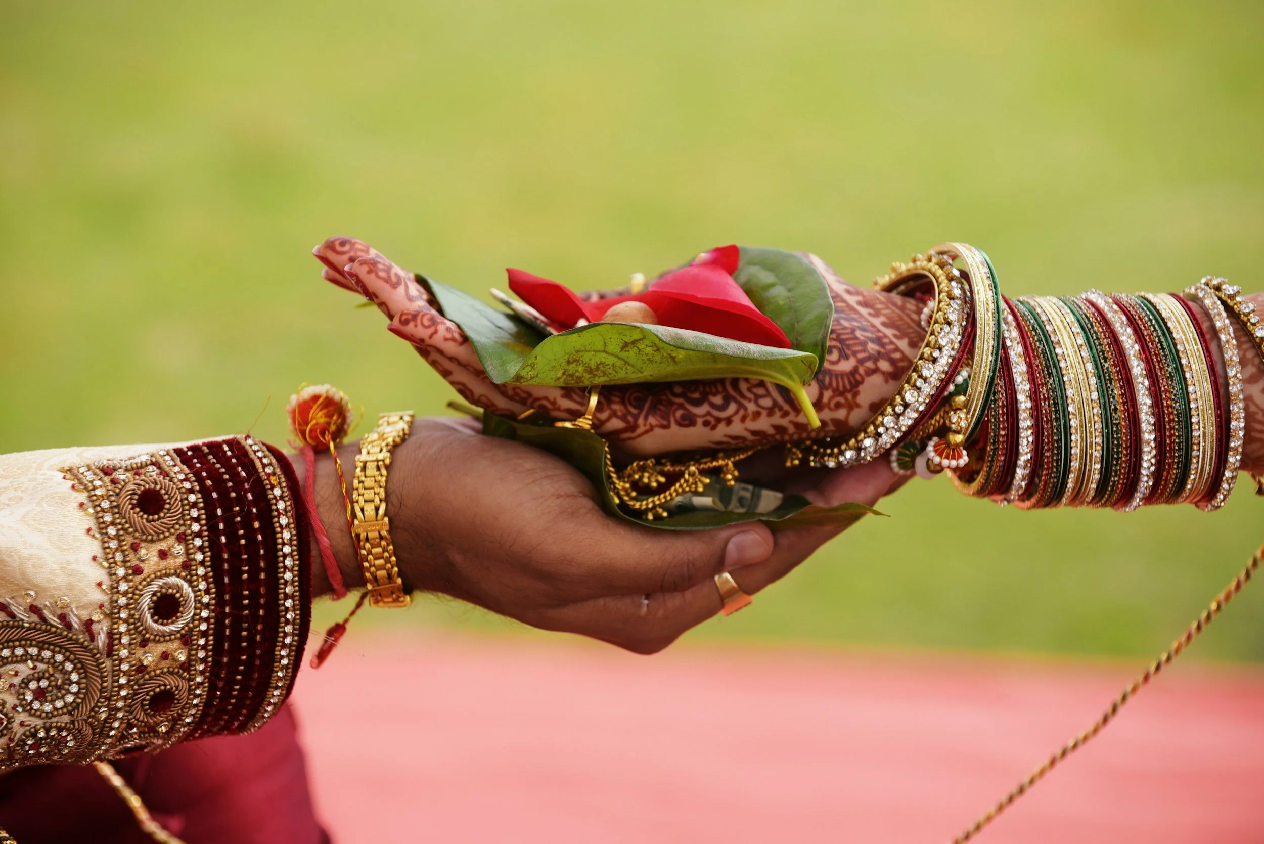 A person dressed in traditional colorful attire holding a flower in their hand, adorned with numerous bangles and jewelry, with a green background.