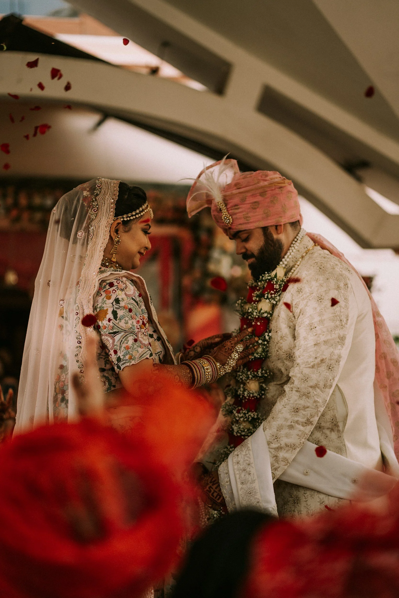 A bride and groom in traditional Indian wedding attire, exchanging wedding garlands, smiling at each other.