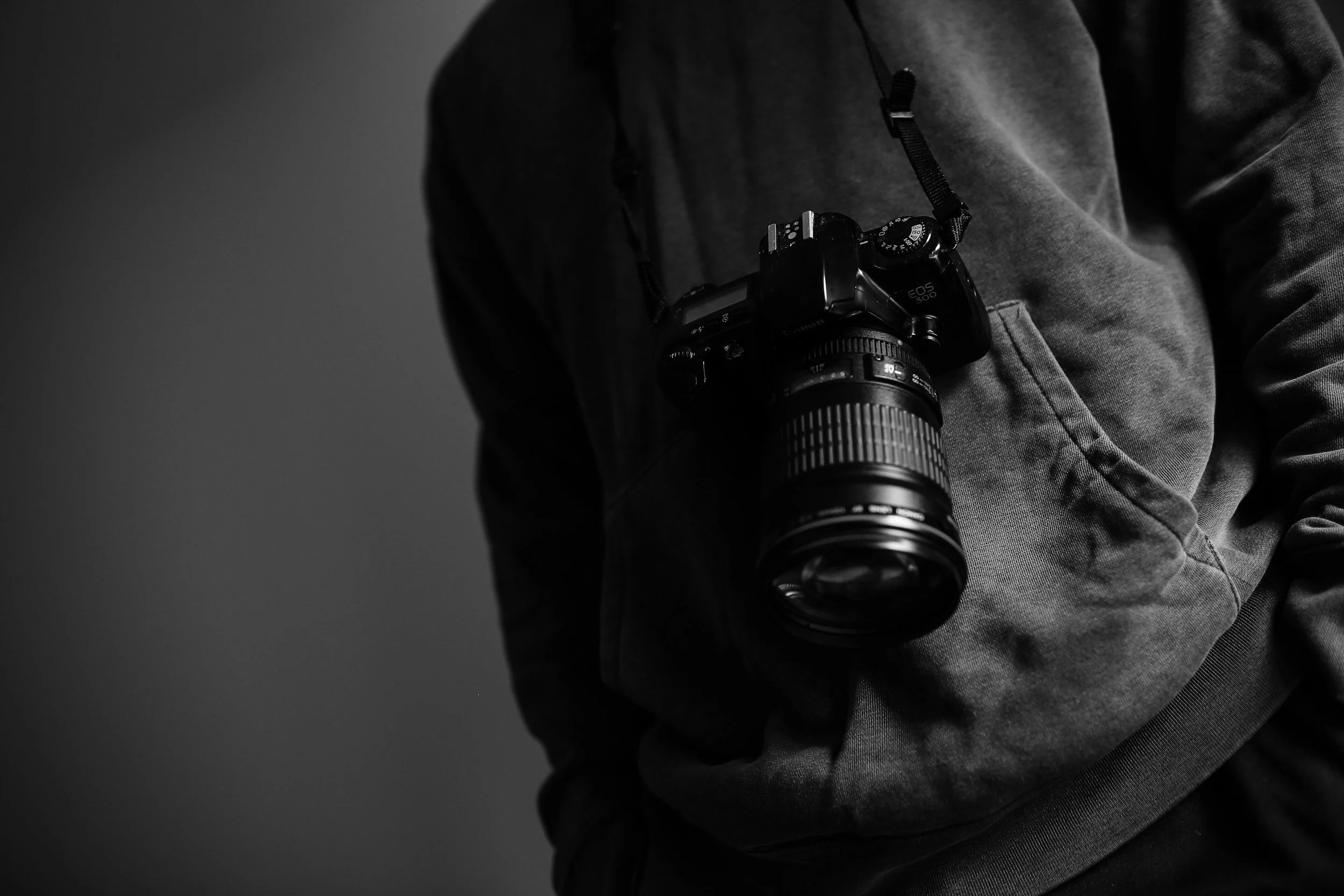Black and white photo of a person wearing a hoodie with a camera hanging around their neck.