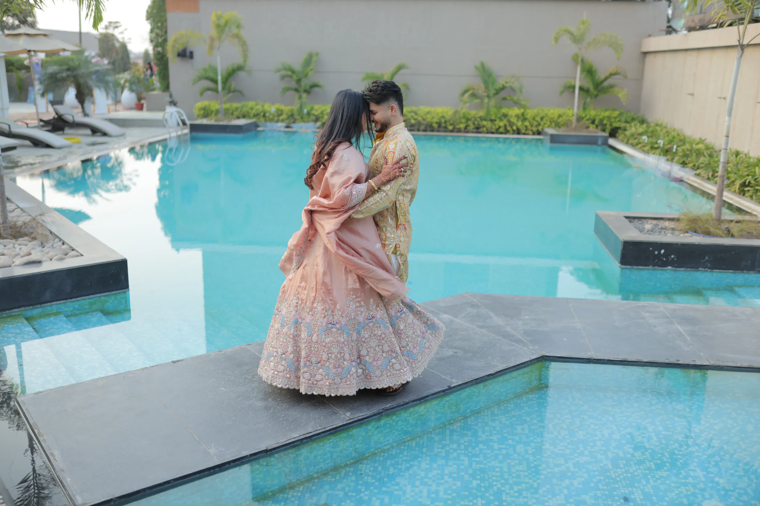 A couple dressed in traditional Indian attire standing close together by a swimming pool, sharing an intimate moment outdoors.