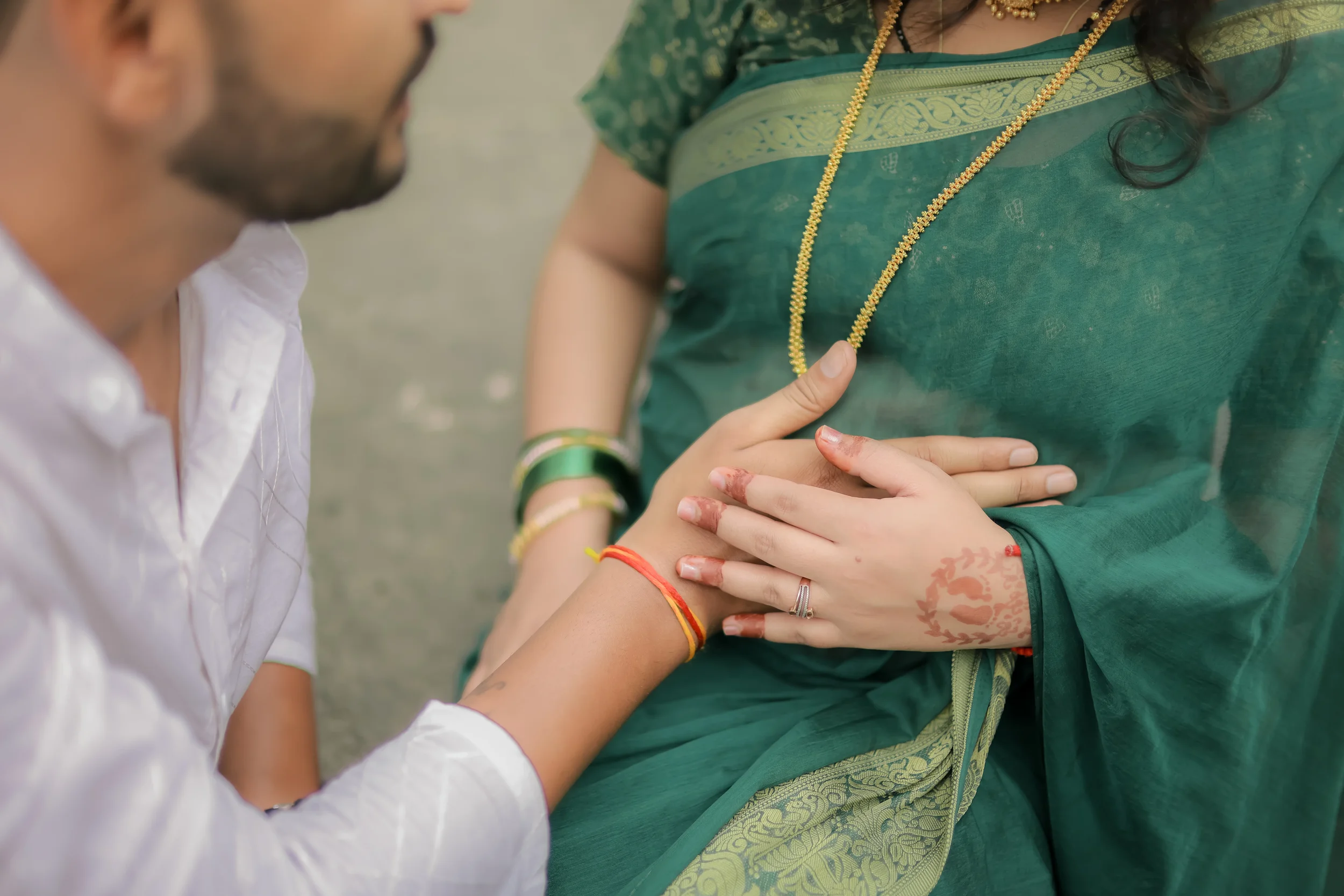A person in traditional Indian attire with jewelry and henna on hands is holding another person's arm, possibly during a ritual or ceremony.