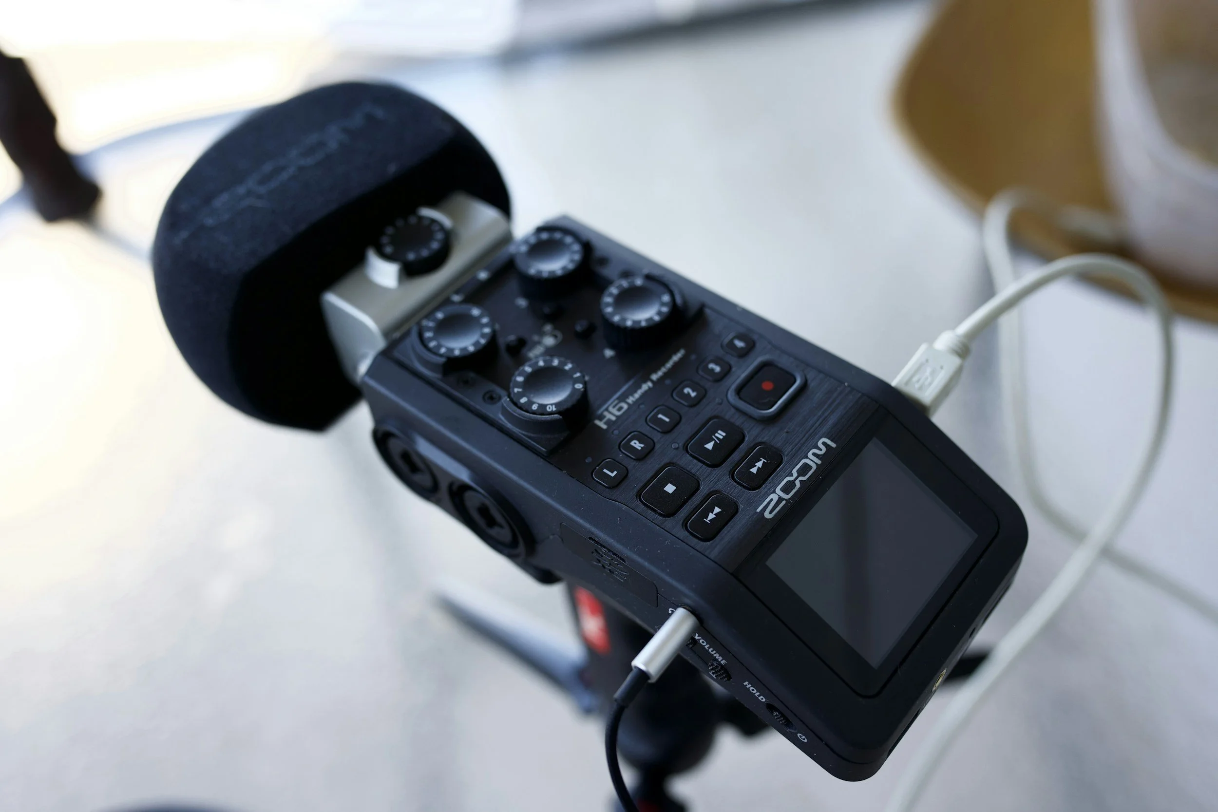 Close-up of a portable audio recorder with attached microphone, hand-held and connected via a white cable.