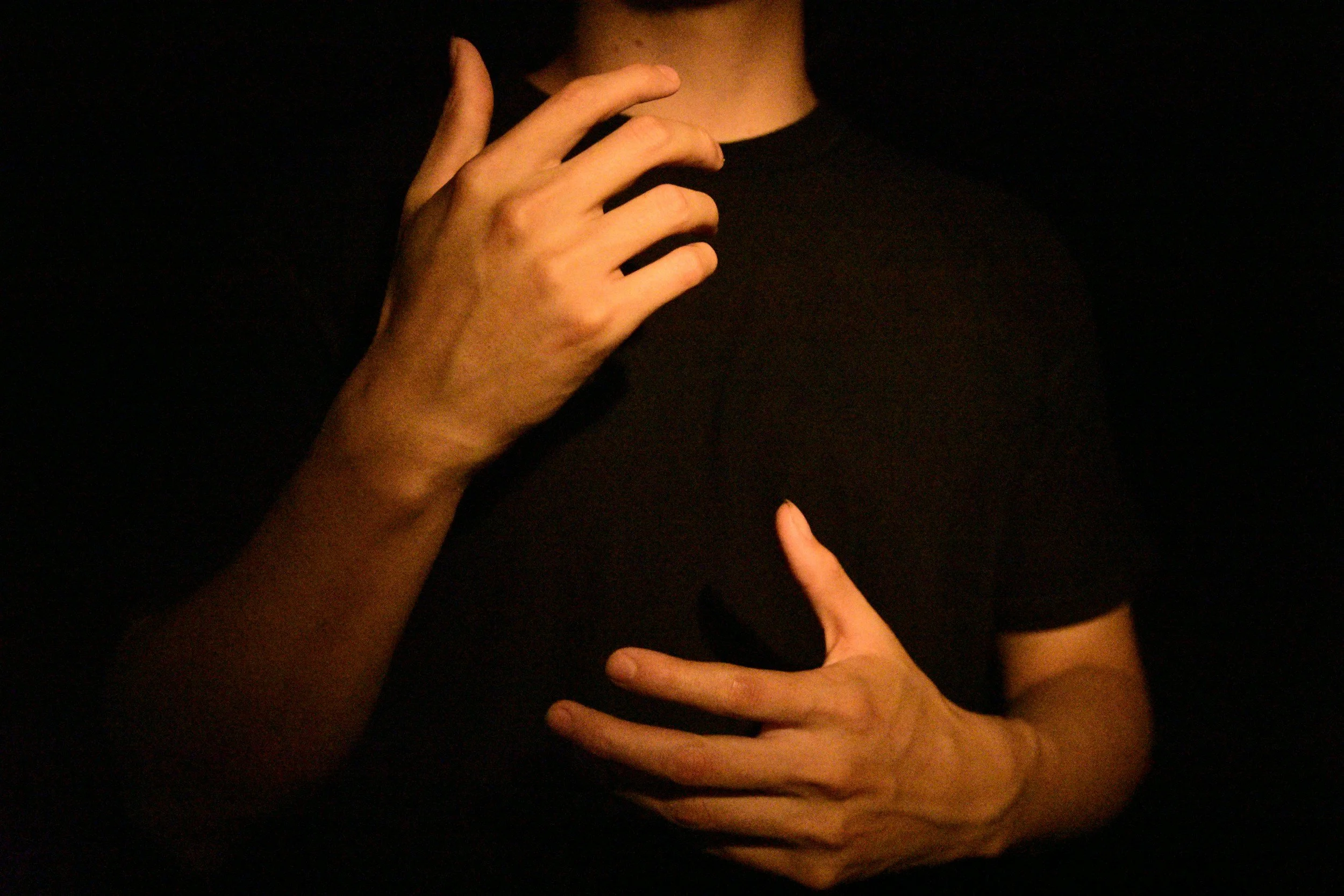 Close-up of a person with dark clothing, holding their hand near their face, with another person's hand touching their chest.