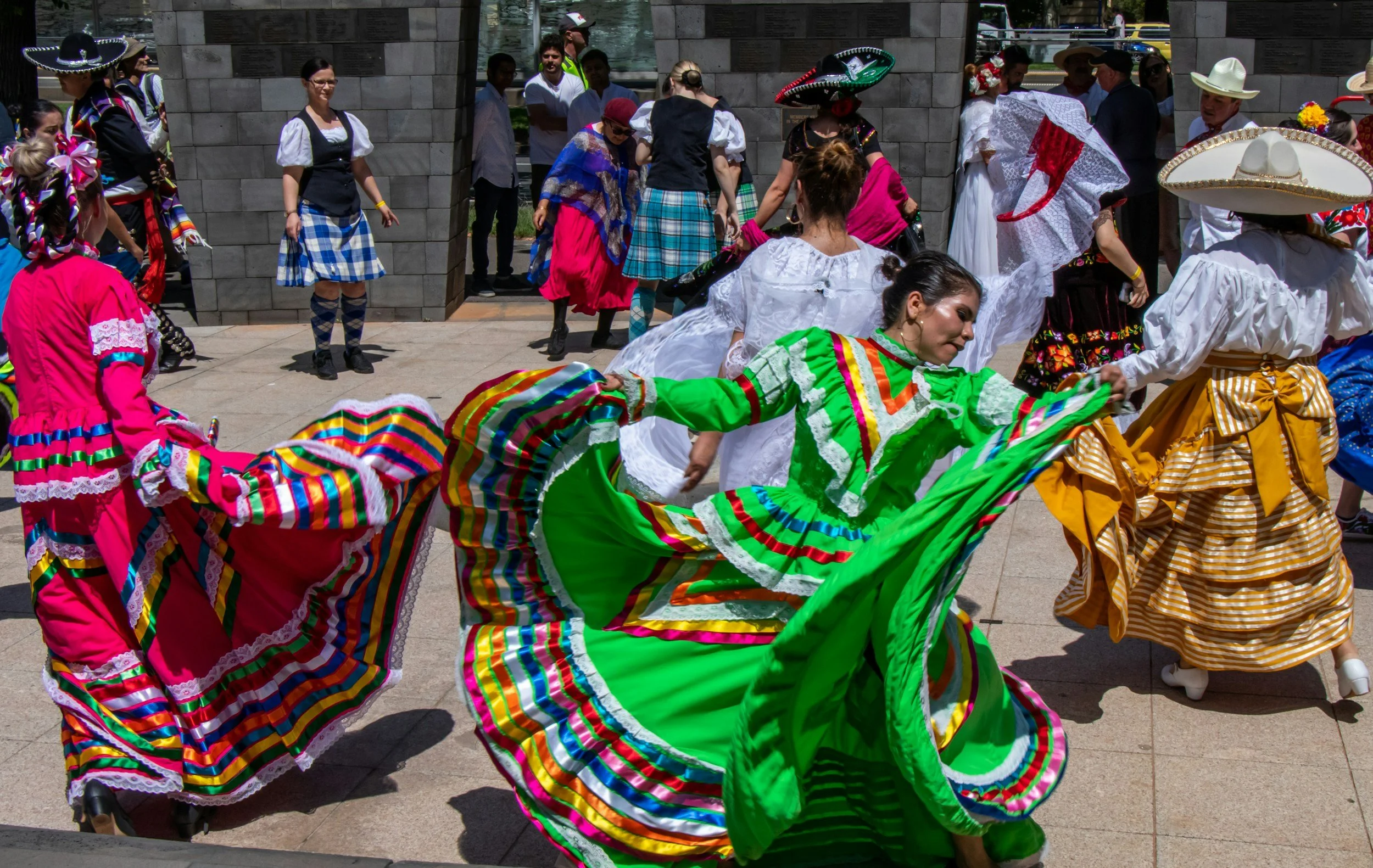 Mexican dancers in colorful traditional dresses performing at an outdoor event with onlookers.