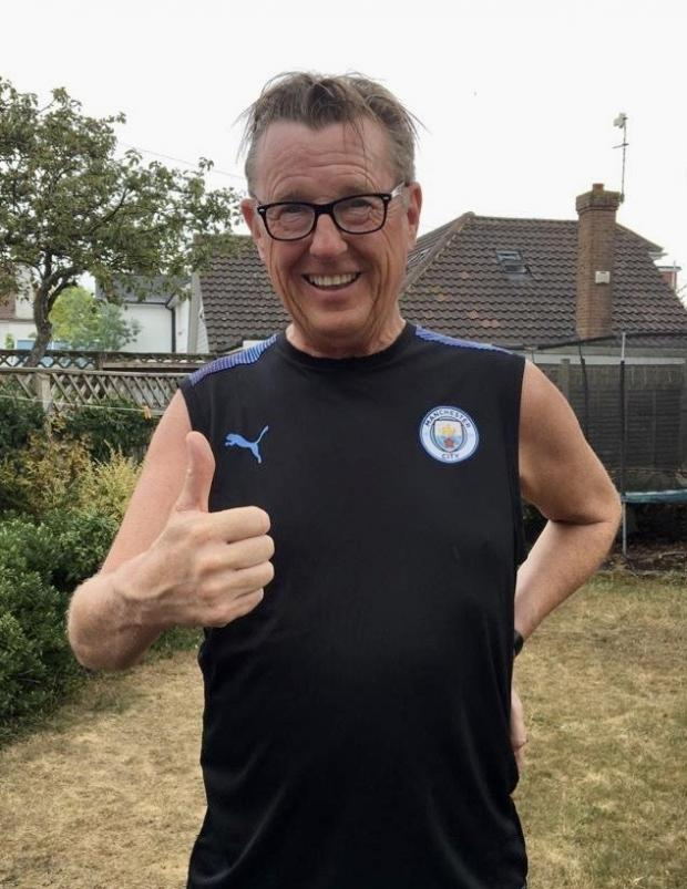 A man wearing glasses and a Manchester City football jersey giving a thumbs up in a backyard.