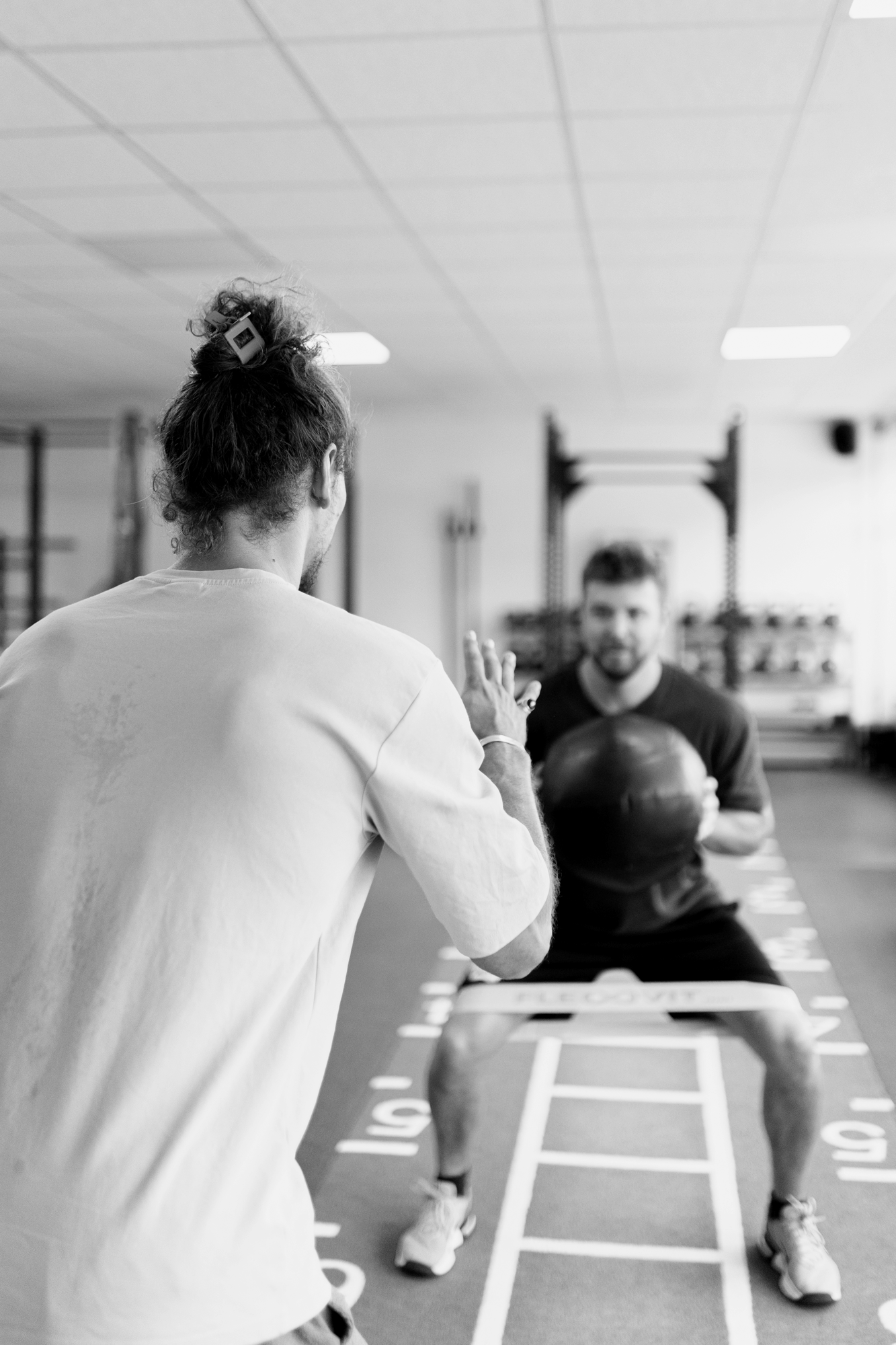 Zwei Männer im Fitnessstudio, die sich auf ein Training vorbereiten. Einer steht, der andere sitzt auf einem Sprint- und Multiball, während sie sich im Bereich für Kraft- und Fitnesstraining befinden.