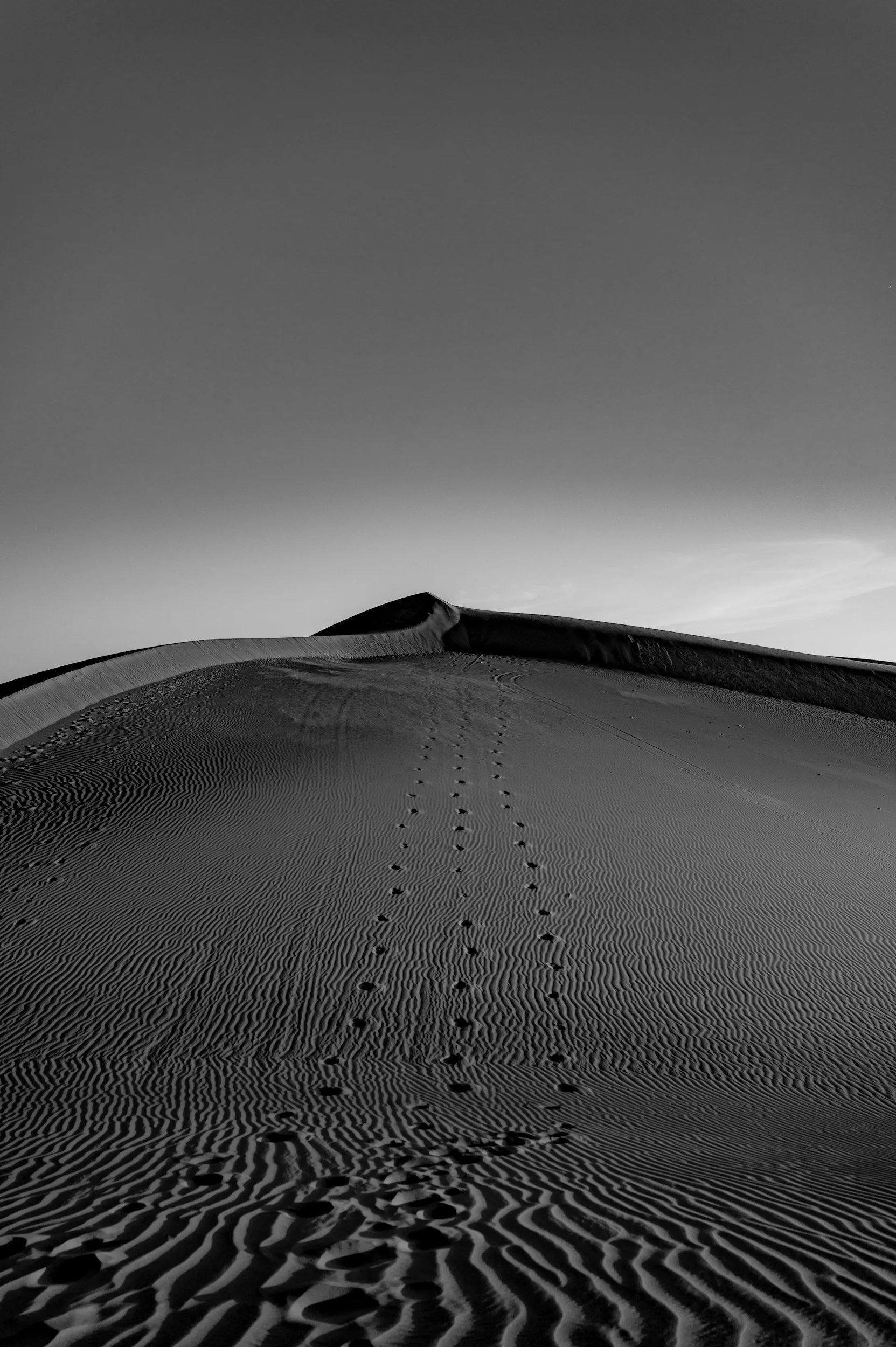 Sanddünen mit Fußspuren und Spuren im Wüstensand, unter einem dunklen Himmel.