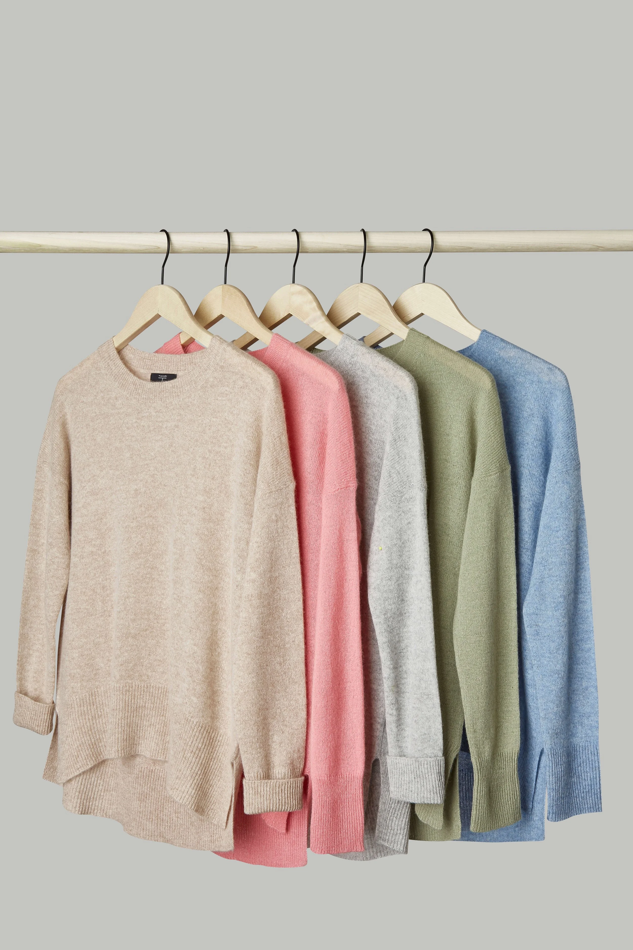 Five sweaters in different colors hanging on a clothing rack.