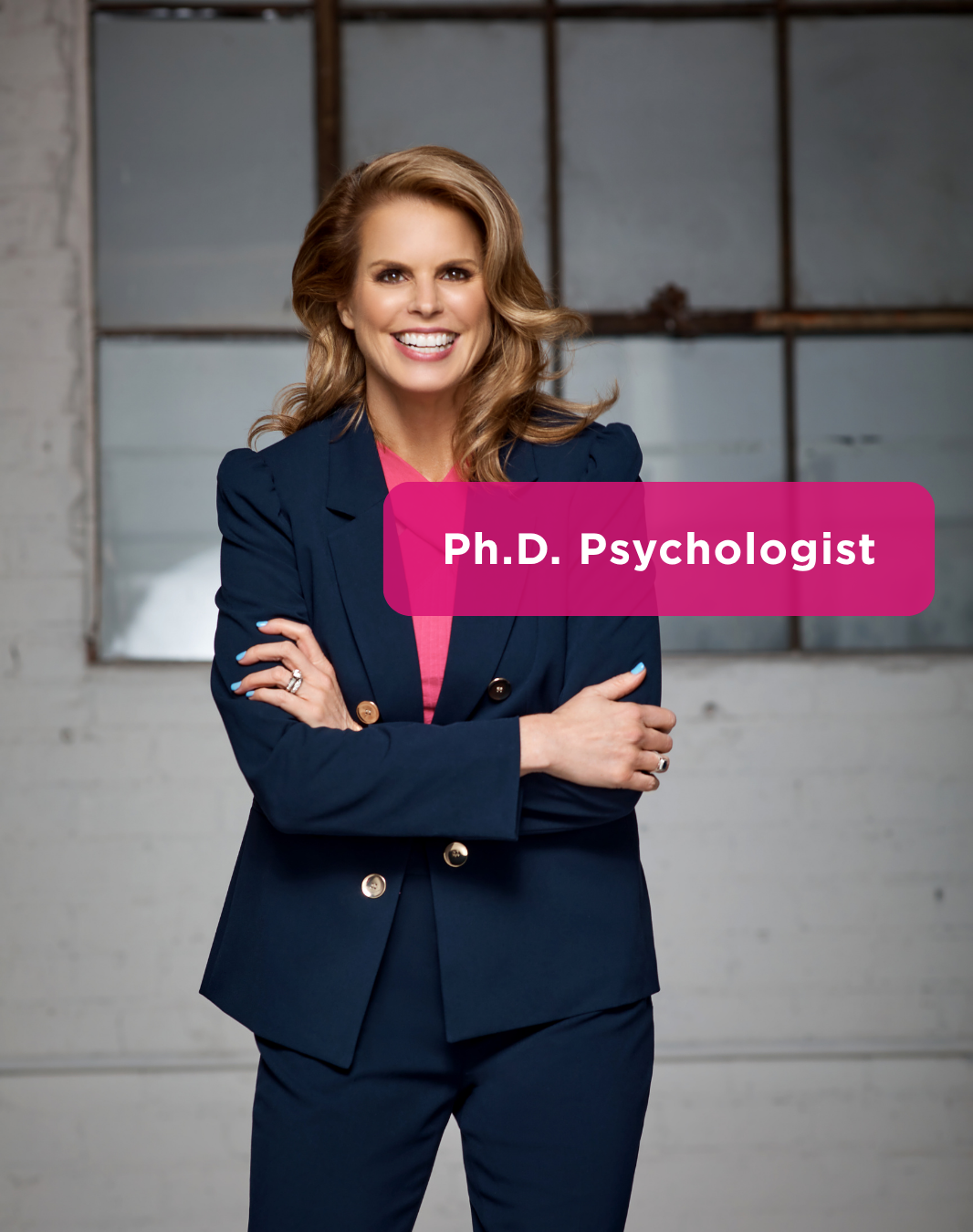 A woman with shoulder-length wavy blonde hair, wearing a navy blue blazer over a pink top, smiling and standing with arms crossed in front of a industrial-style background with a large window. Text overlay reads 'Ph.D. Psychologist' in pink box.