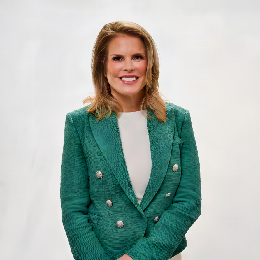 A woman with shoulder-length blonde hair smiling, wearing a teal blazer with silver buttons over a white top, standing against a plain white background.