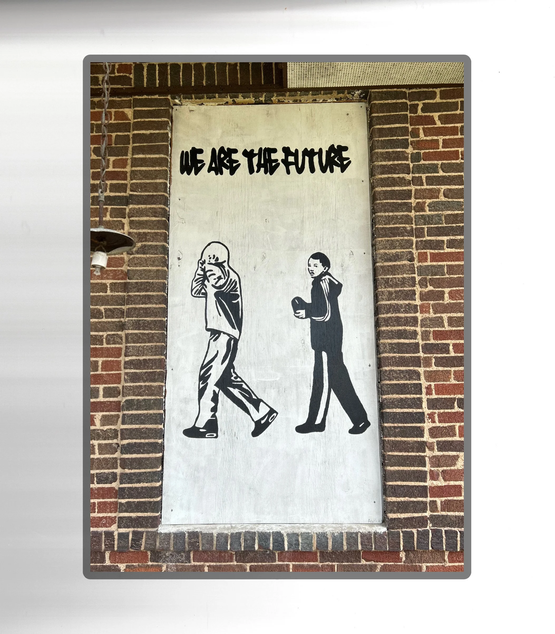 Graffiti art showing a man and a woman, with a caption reading "We Are The Future," on a brick wall background.