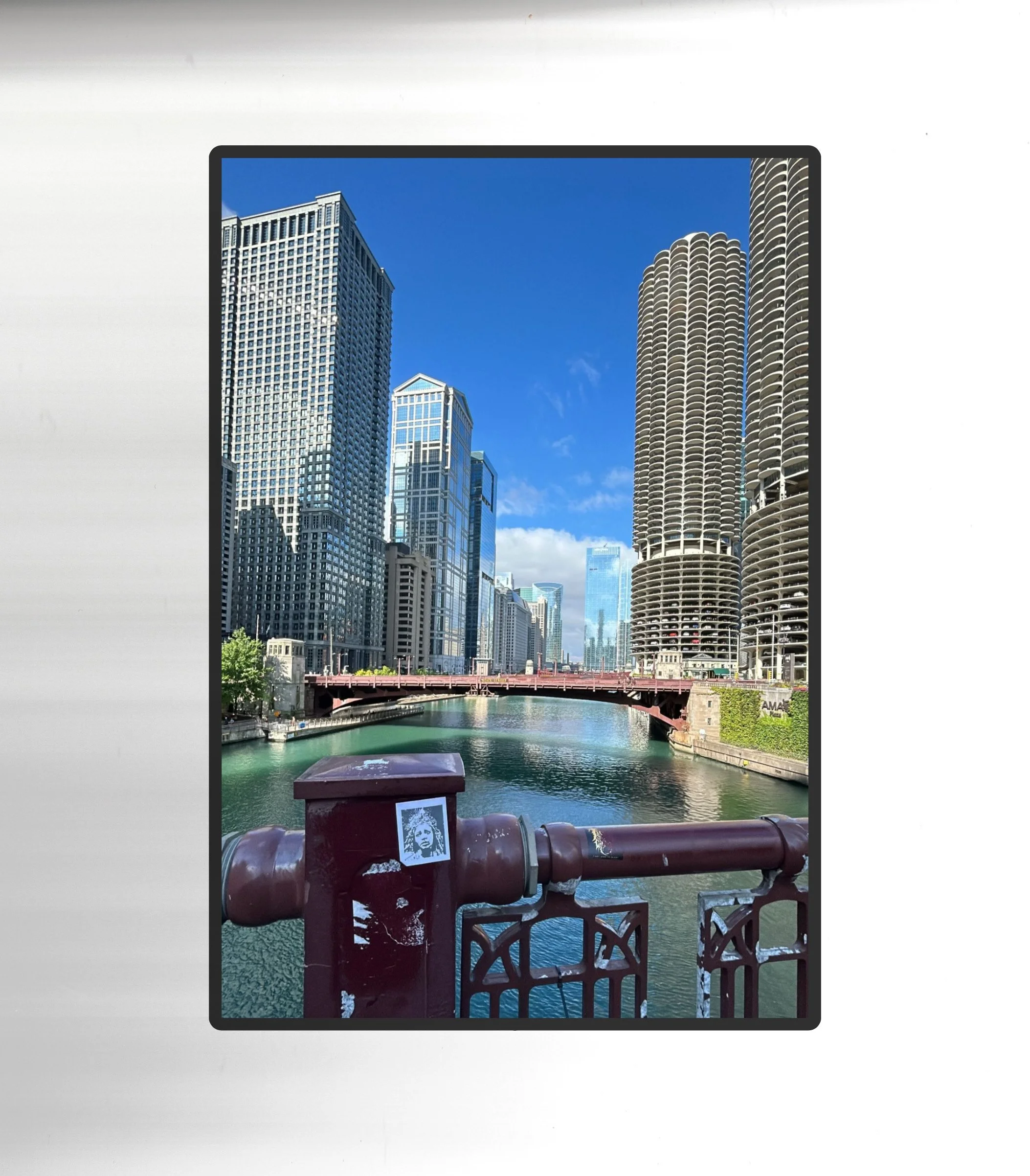 City skyline with high-rise buildings along a river, viewed from a bridge with a red railing and a stencil of Martin Luther King Jr. on a pipe in the foreground.
