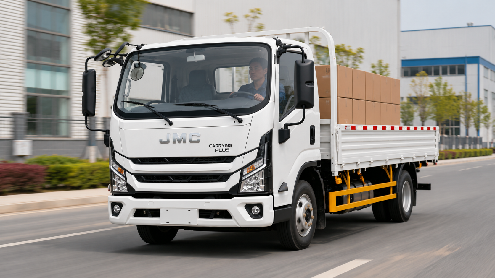 White JMC Carrying Plus flatbed truck with cardboard boxes driving on an urban road.