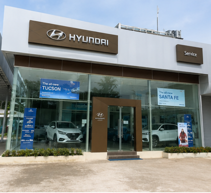 Hyundai car dealership with a glass storefront displaying cars inside, Hyundai logo and signage, and advertisements for Tucson and Santa Fe models.