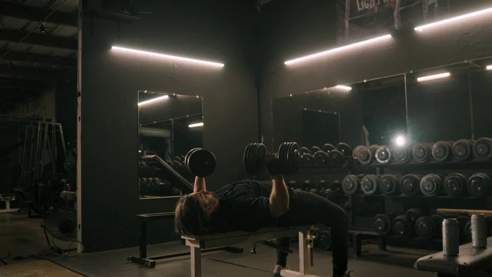 The Forge gym promo still, bench press under strip lights