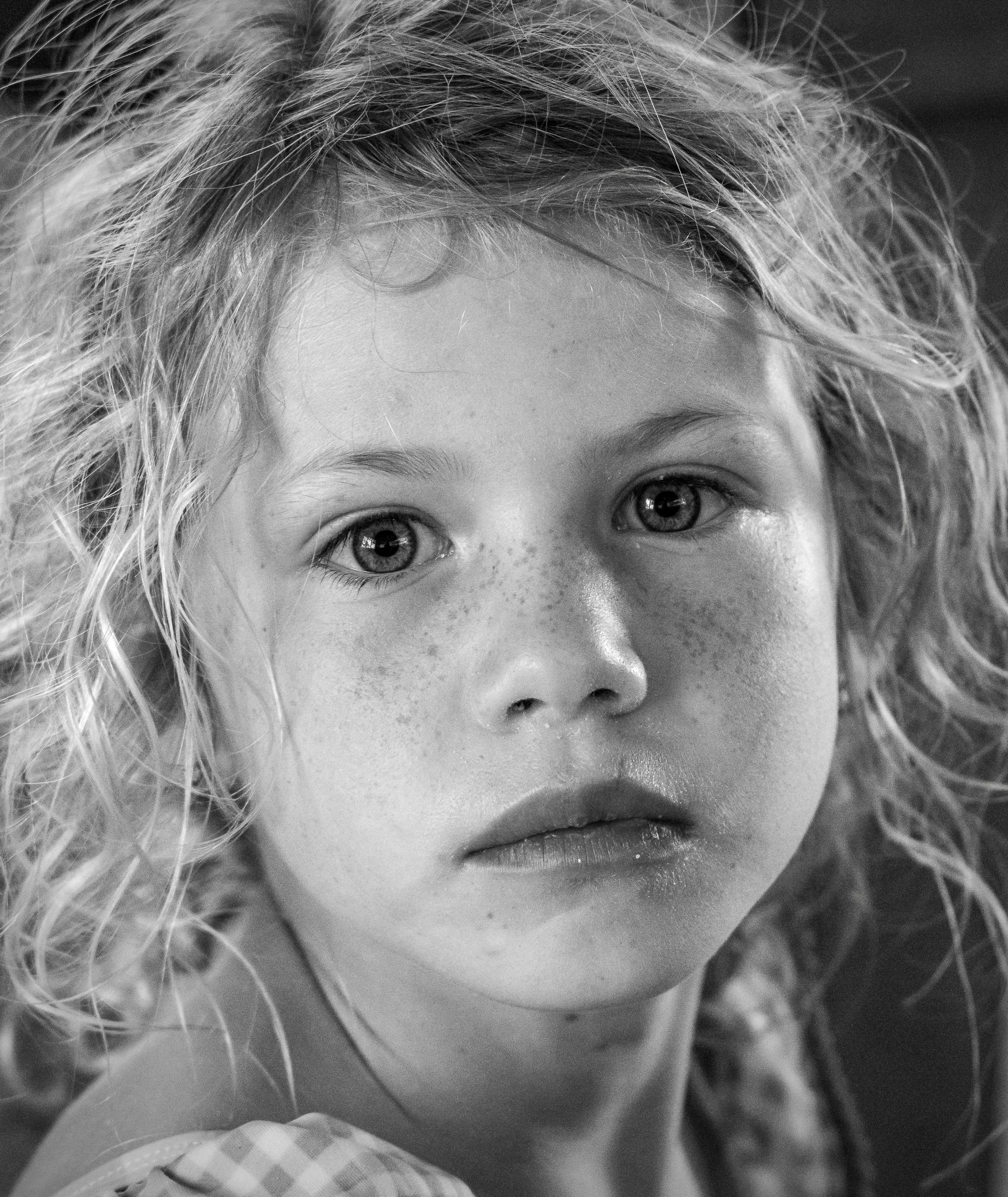 Close-up black and white photo of a child's face, focusing on their eyes, nose, and curly hair.