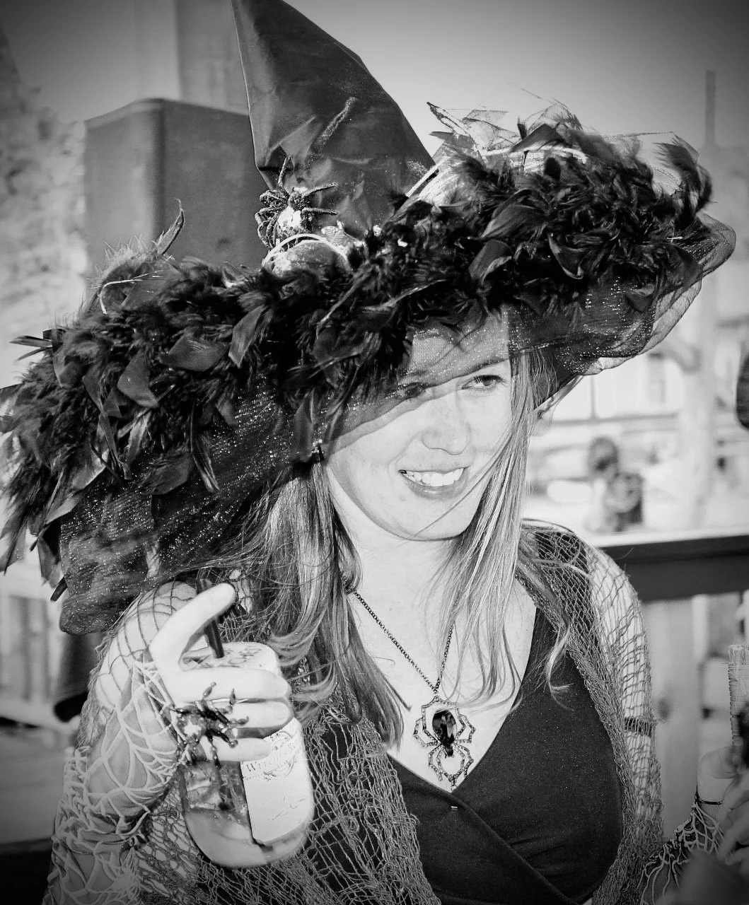 Woman wearing a large feathered hat, smiling, in a festive or costume setting.