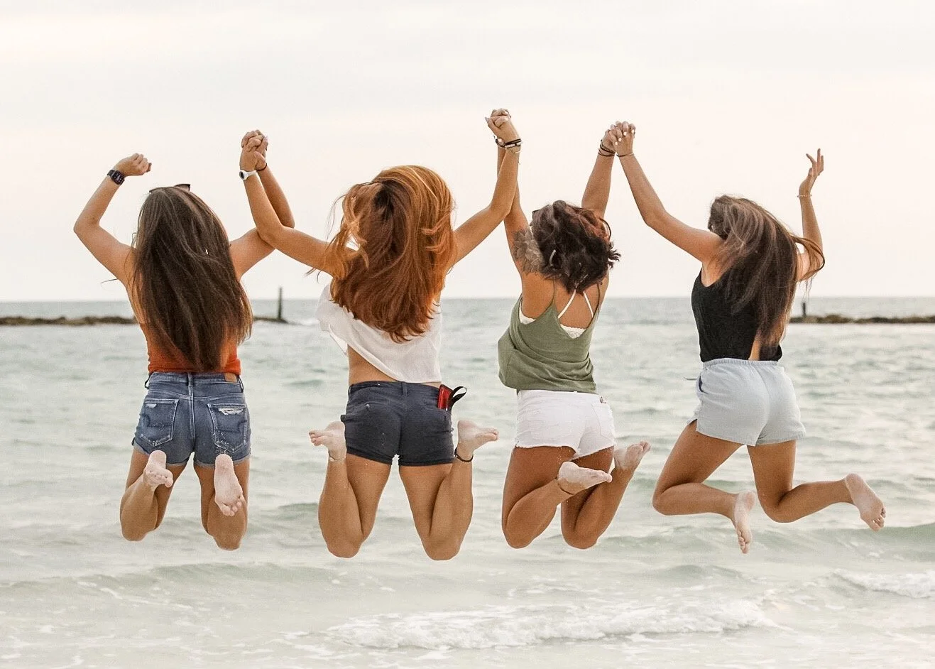 Four women jumping on the beach with the ocean and sky in the background.