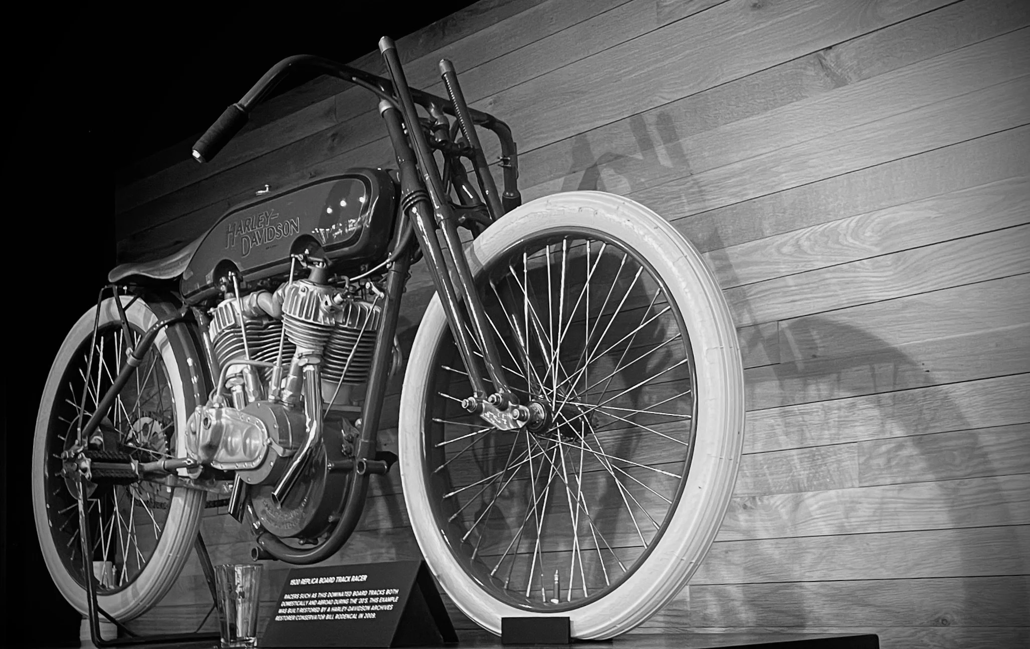 A vintage Harley-Davidson motorcycle on display against a wooden wall, shown in black and white.