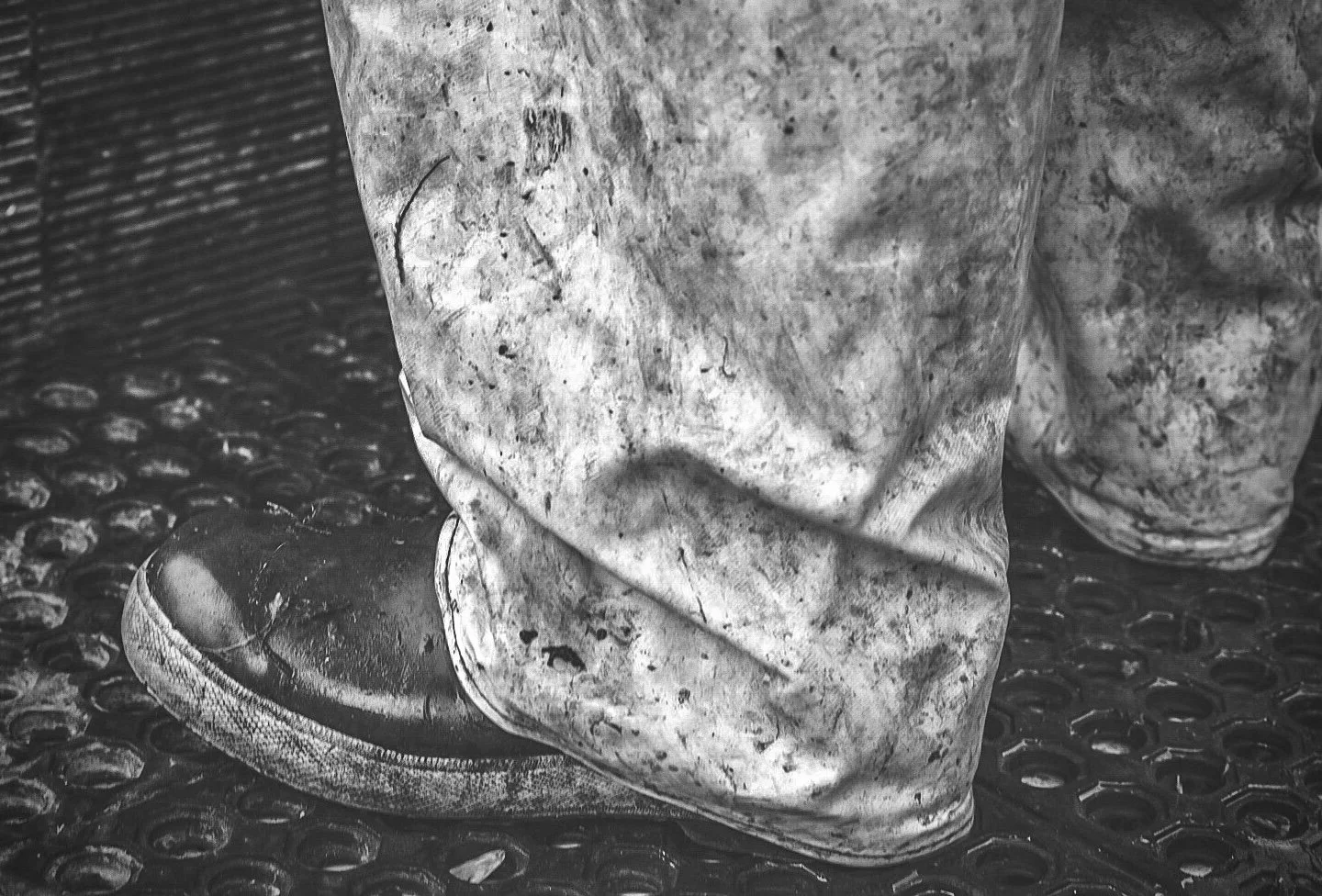 Close-up of a person's worn, dirty shoe resting on a textured rubber surface, with the person's dirty pants visible.