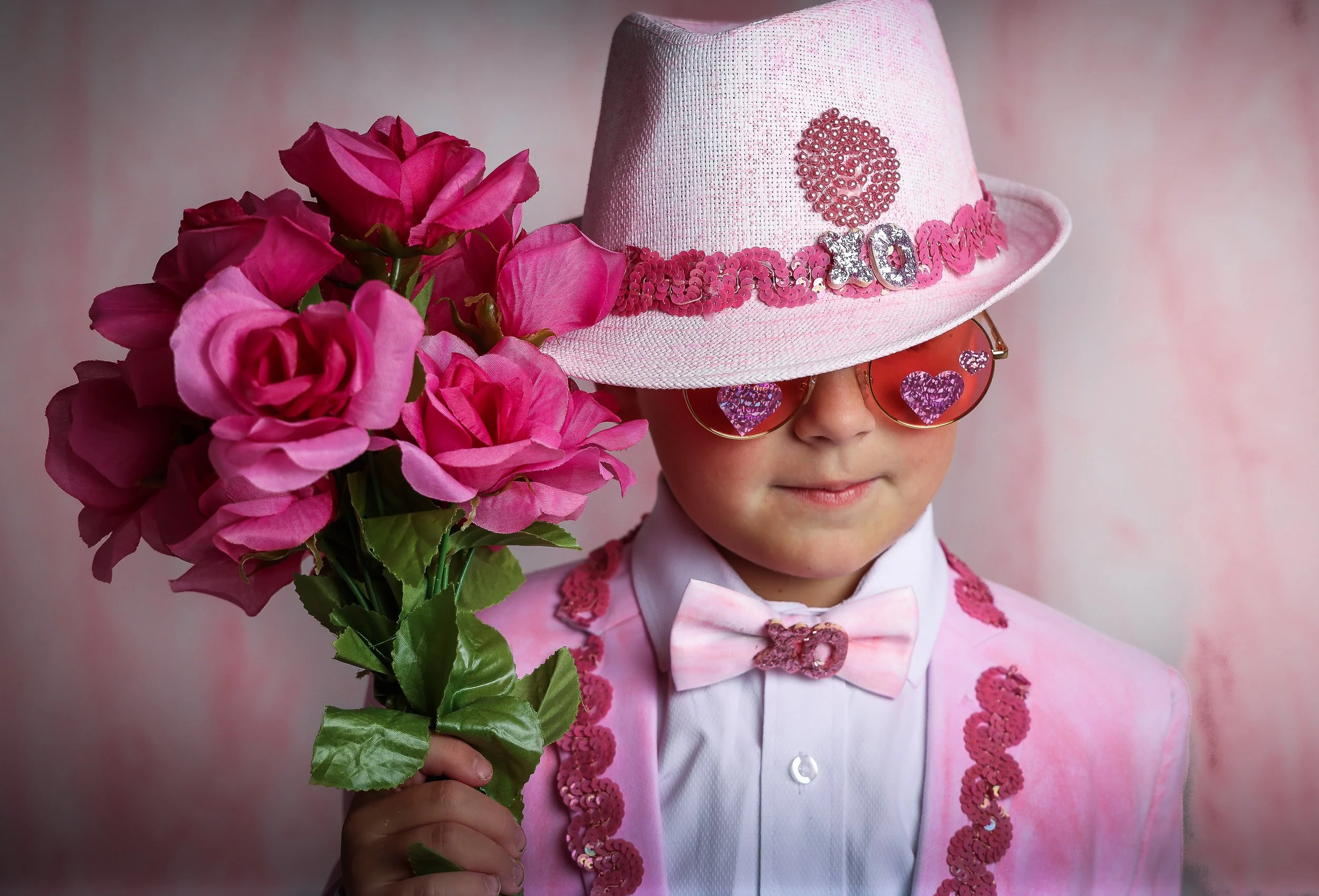 A child in a pink sequined hat and pink suit holding a bouquet of pink flowers.