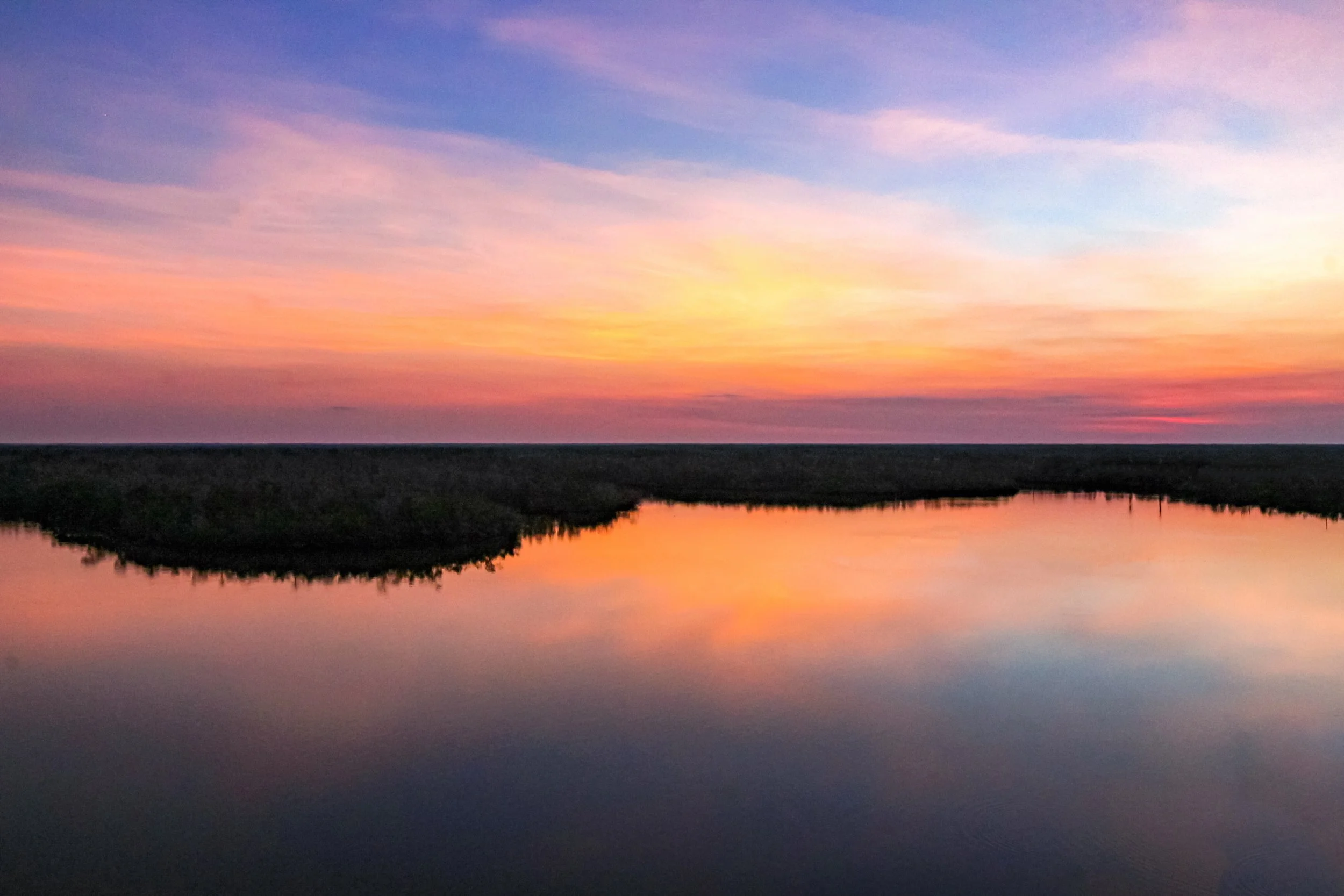 A colorful sunset over a calm river with a small island or landmass in the foreground.