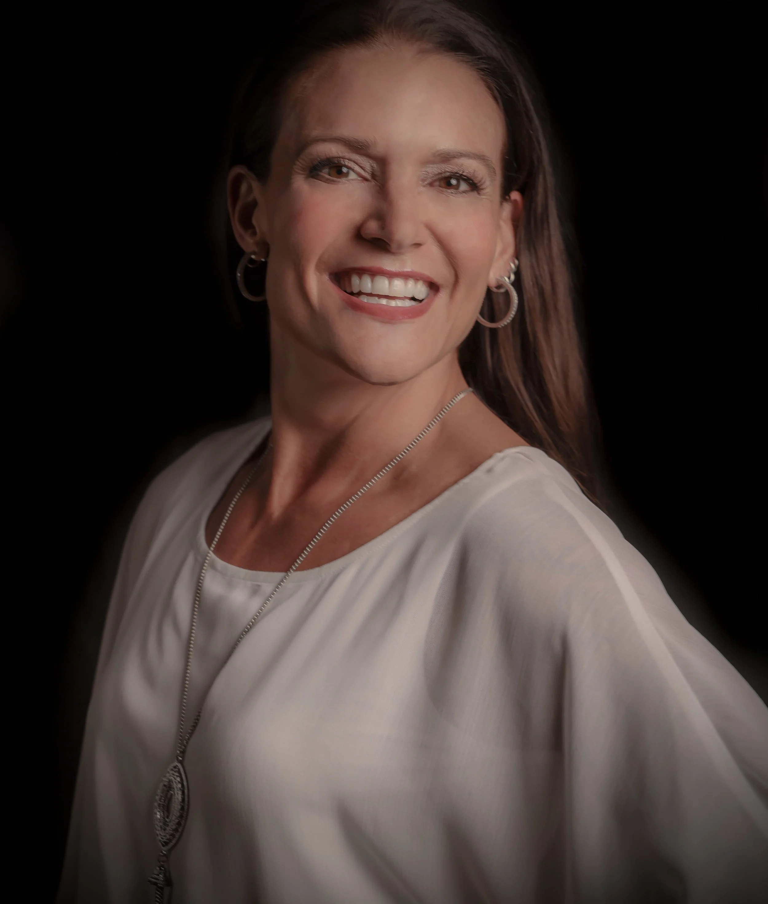 Smiling woman with earrings and a light-colored zip-up top, posing against a black background.