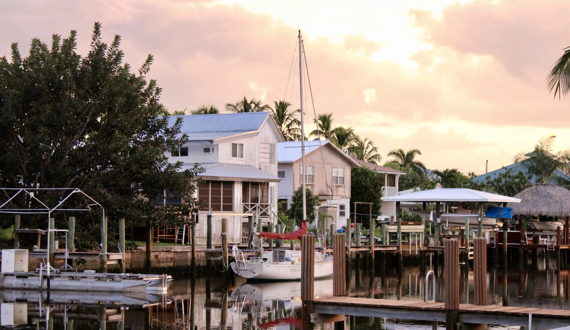 A waterfront scene at sunset with houses, boats, and lush palm trees.
