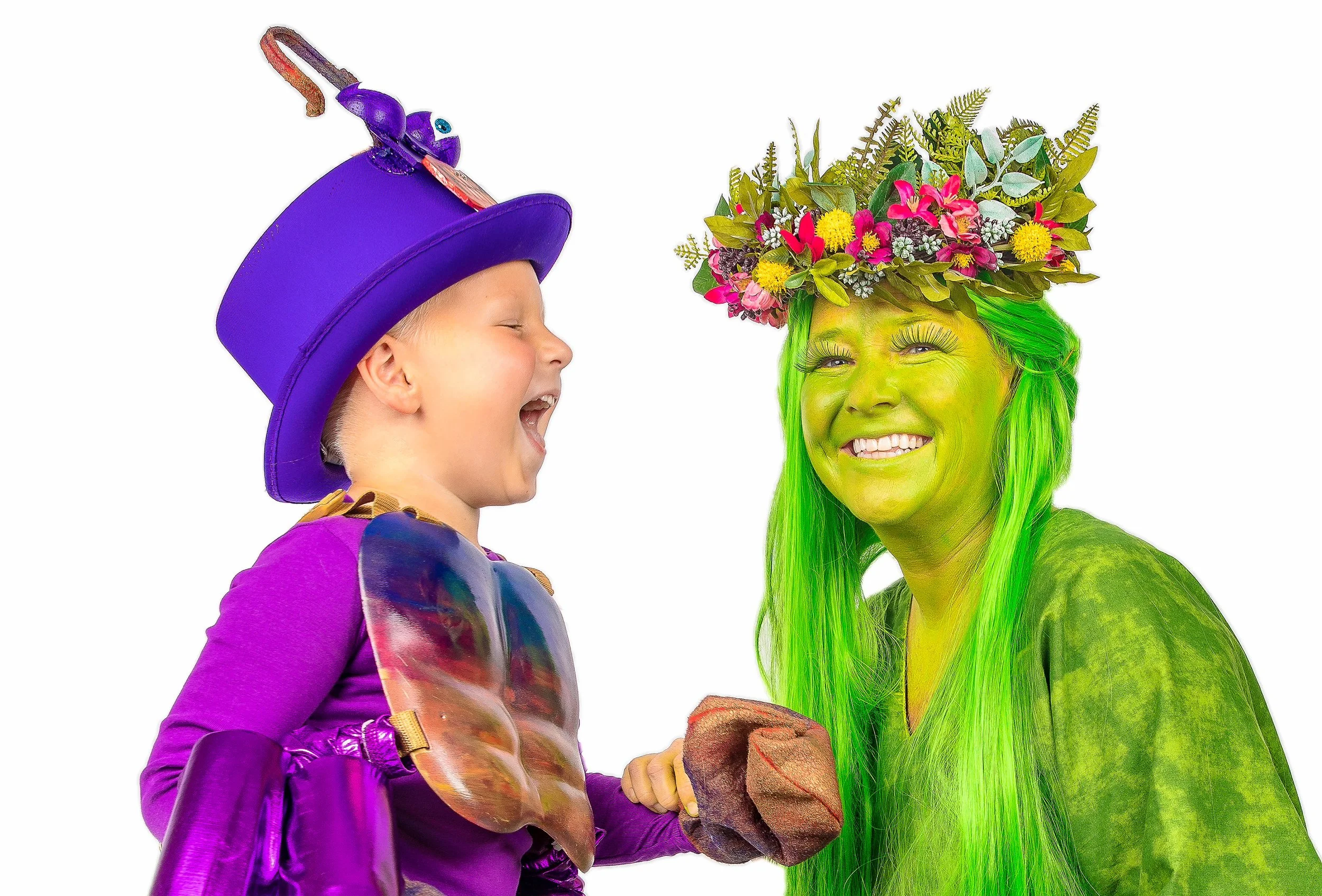 A young child and a woman dressed as a colorful, nature-inspired character smiling and holding hands, with the woman wearing green face paint and a floral headdress.