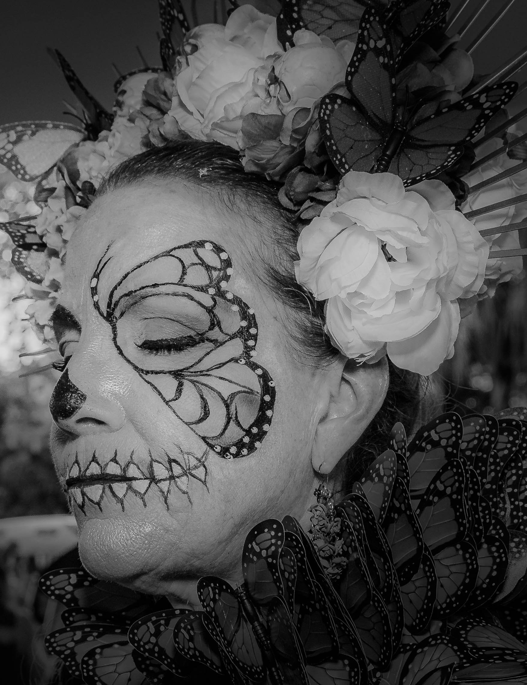 A woman with face paint resembling a sugar skull, surrounded by artificial butterflies and a floral headdress.