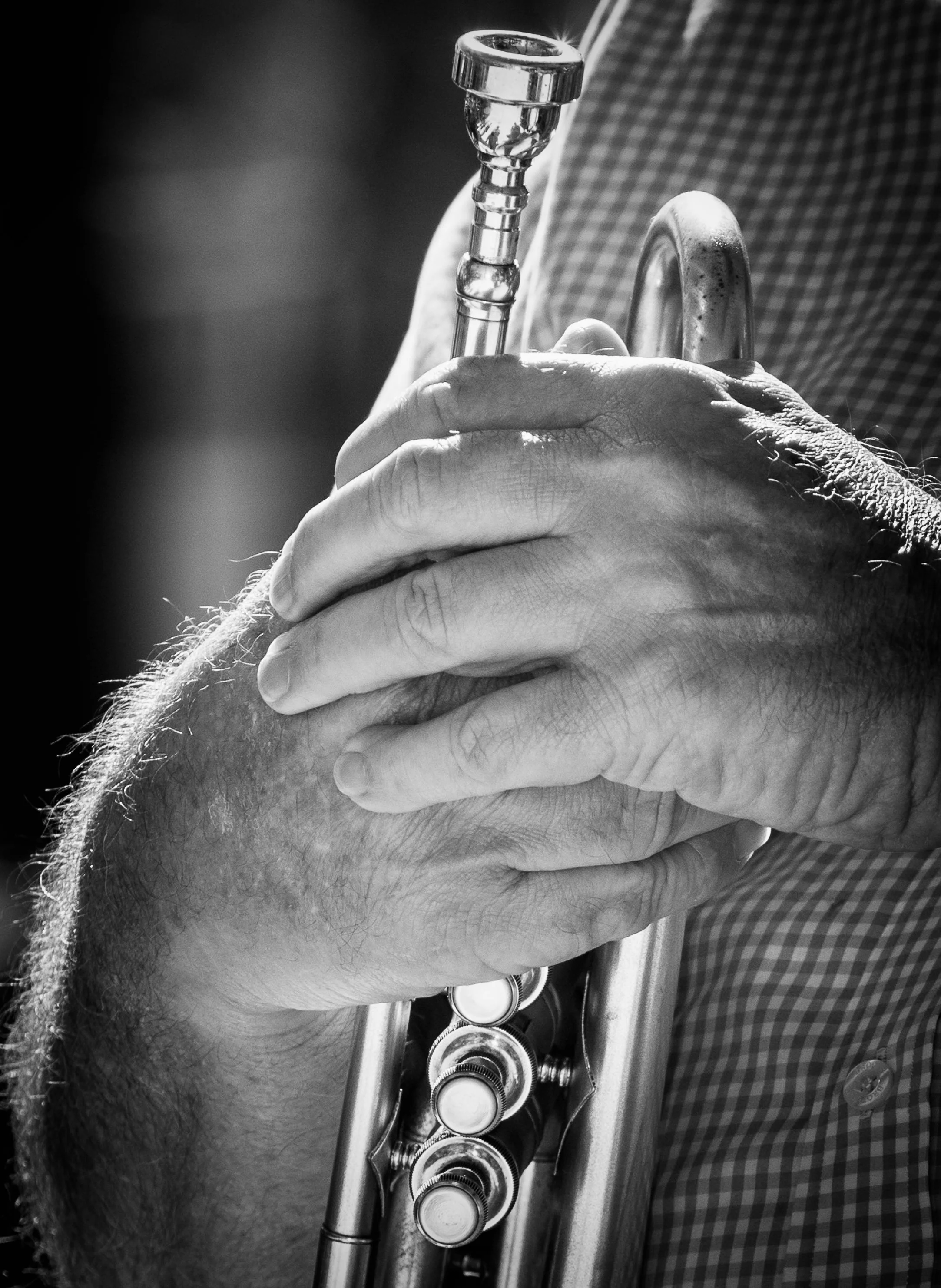 Close-up of a person playing a trumpet, with hands gripping the instrument and valves visible, in black and white.