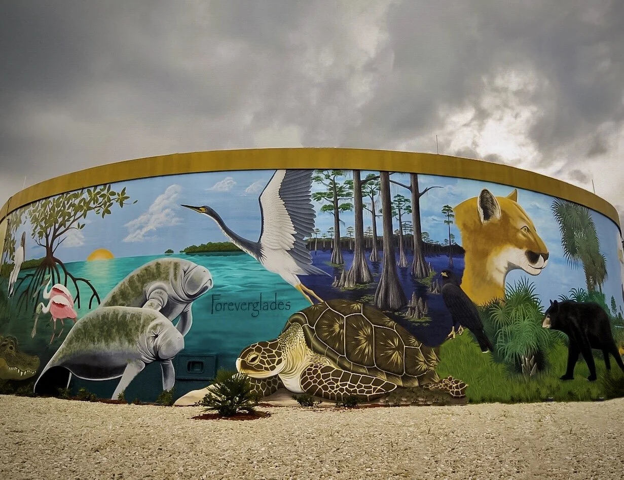 Colorful mural depicting animals of a swamp and rainforest, including two manatees, a heron, a turtle, a black bear, and various trees and water scenes.