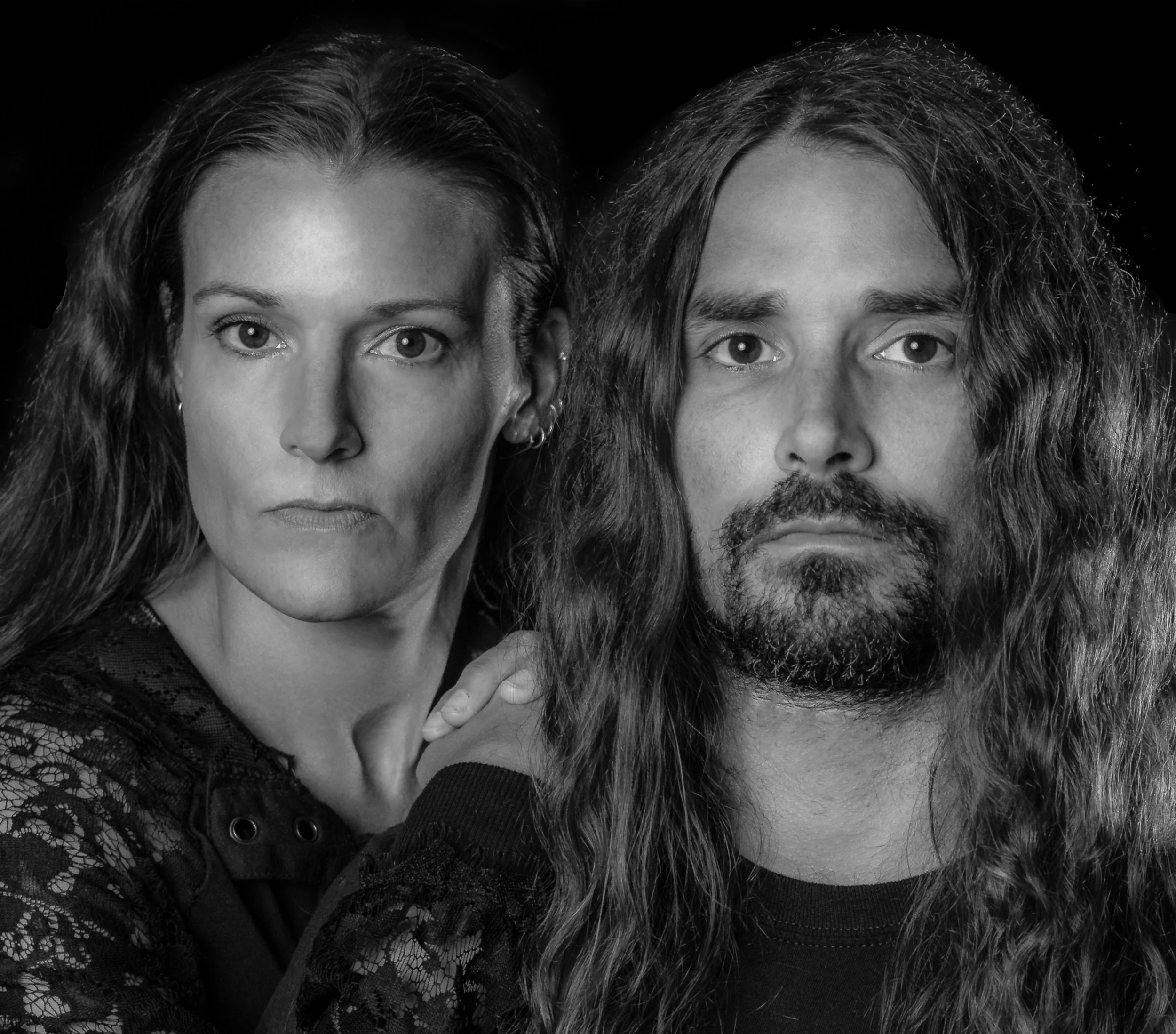 Black and white close-up photograph of a woman and a man with similar hair and eye color, looking directly at the camera. The woman's hair is curly and she wears earrings, and she has a confident expression. The man has long hair and a beard, and a s