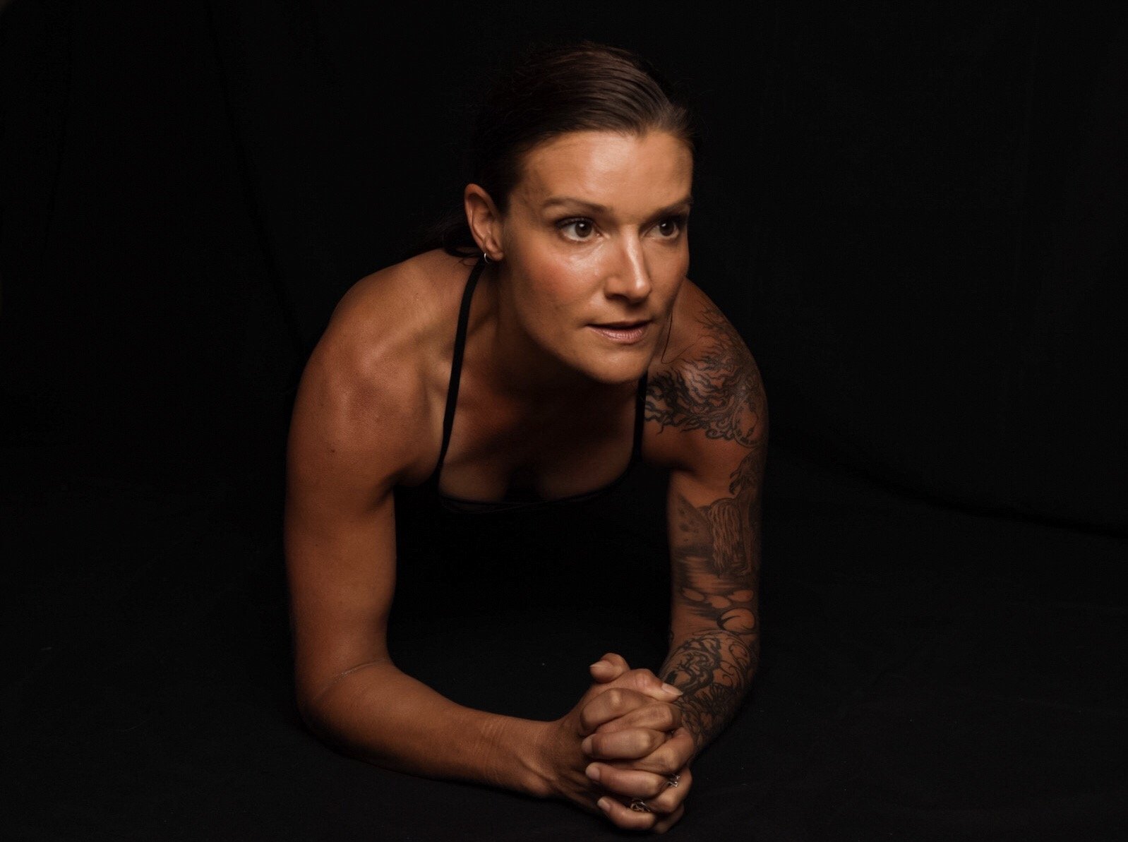 Woman in black tank top doing a plank exercise on a black background