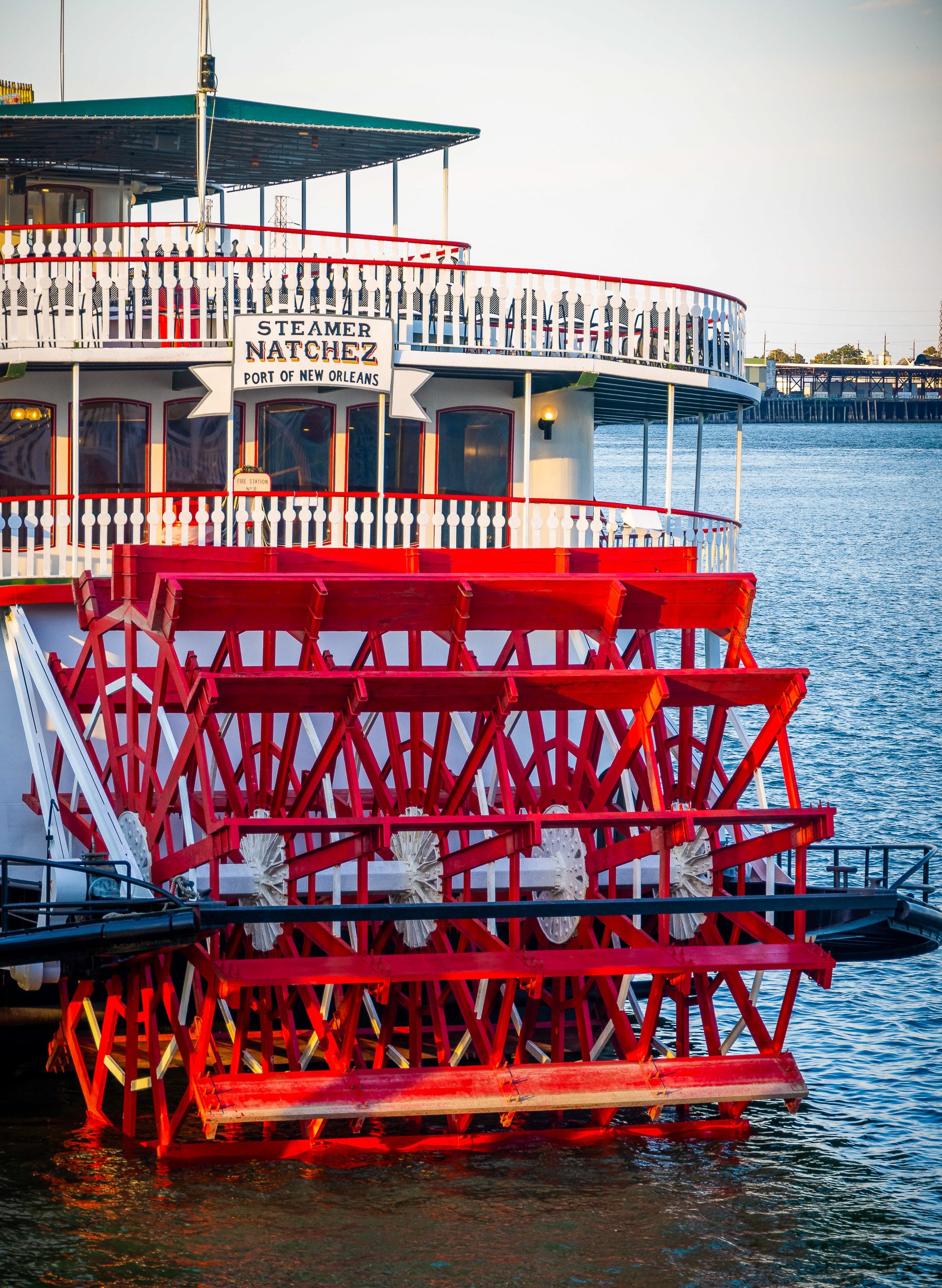 Colorful steamboat with multiple decks and red paddle wheels on the water at sunset in New Orleans.