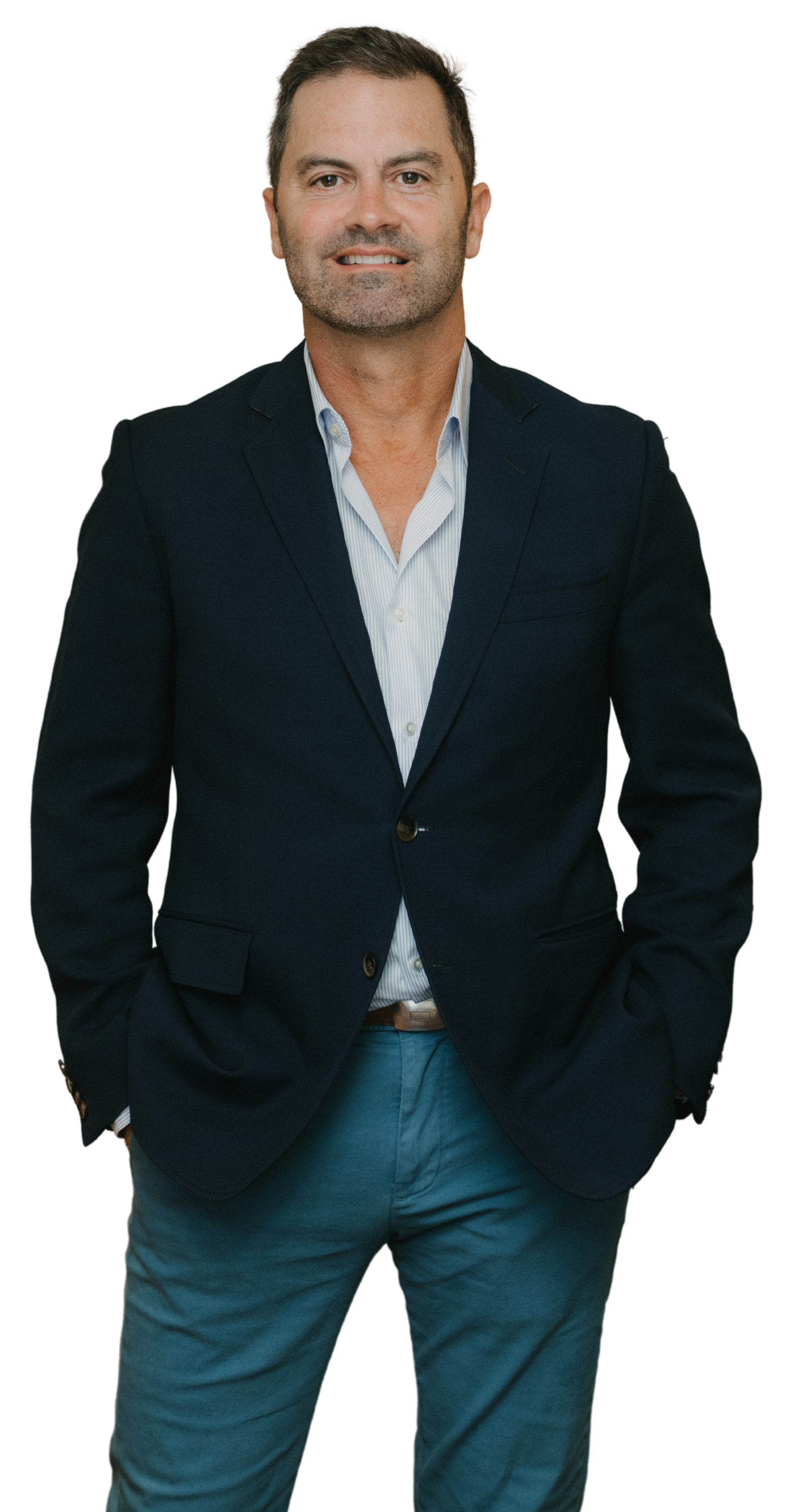 A man in a dark blazer and light blue dress shirt posed with his hands in his pockets, against a black background.