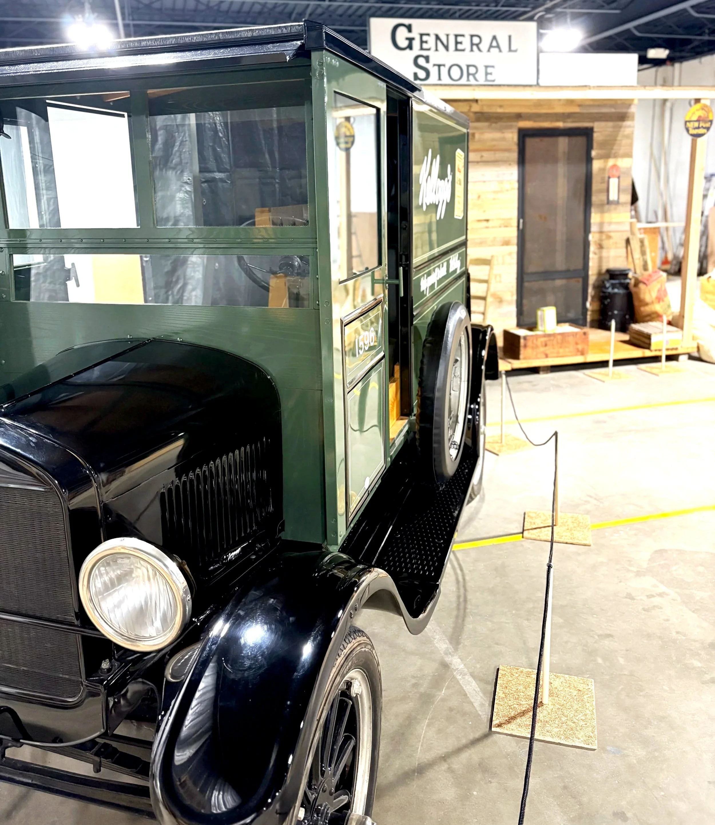 Vintage black vehicle with green wooden cargo box displayed at an indoor expo with a sign that reads "General Store" in the background.