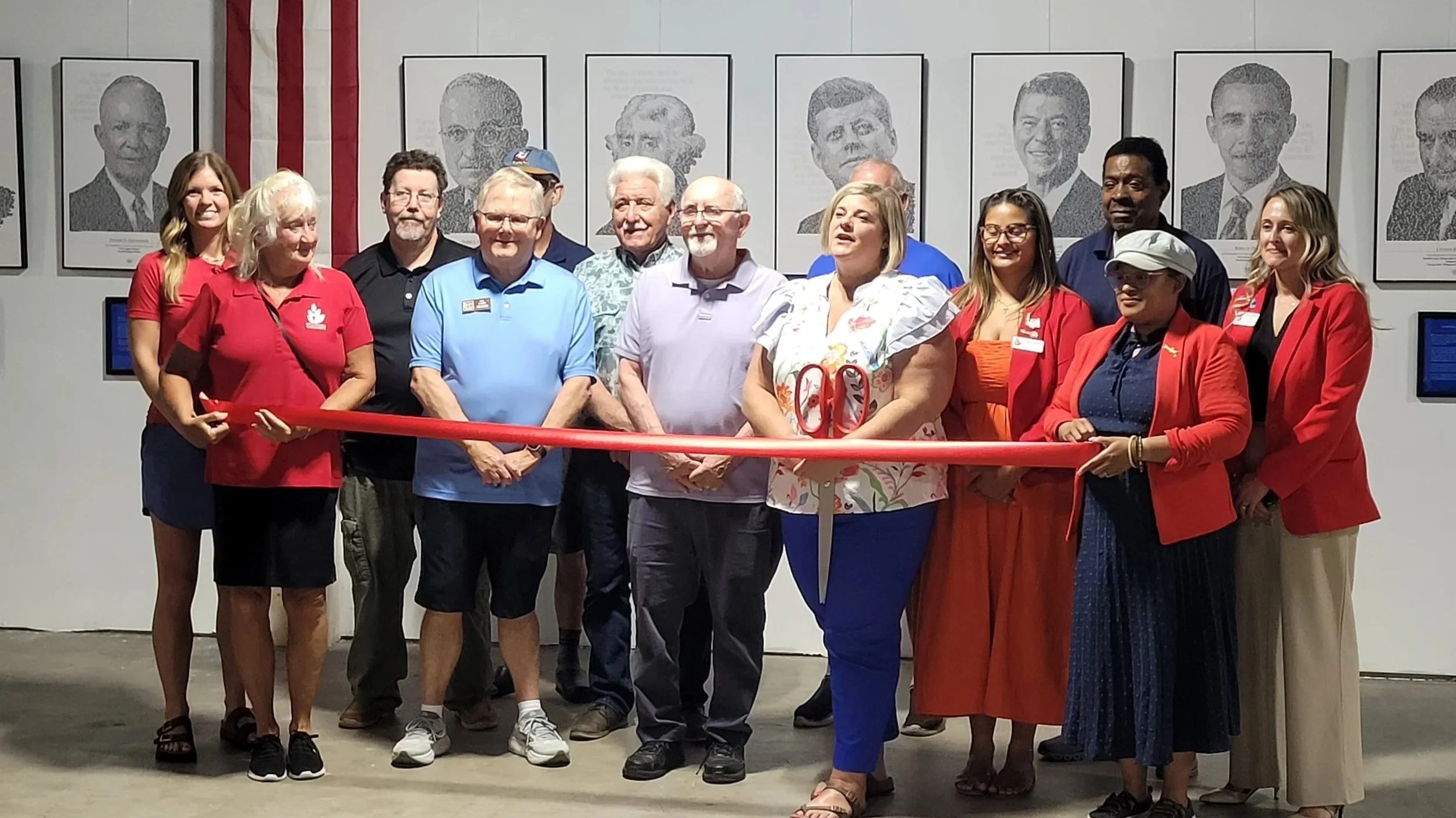 A group of people at a ribbon-cutting event in front of framed historical photos on a wall.