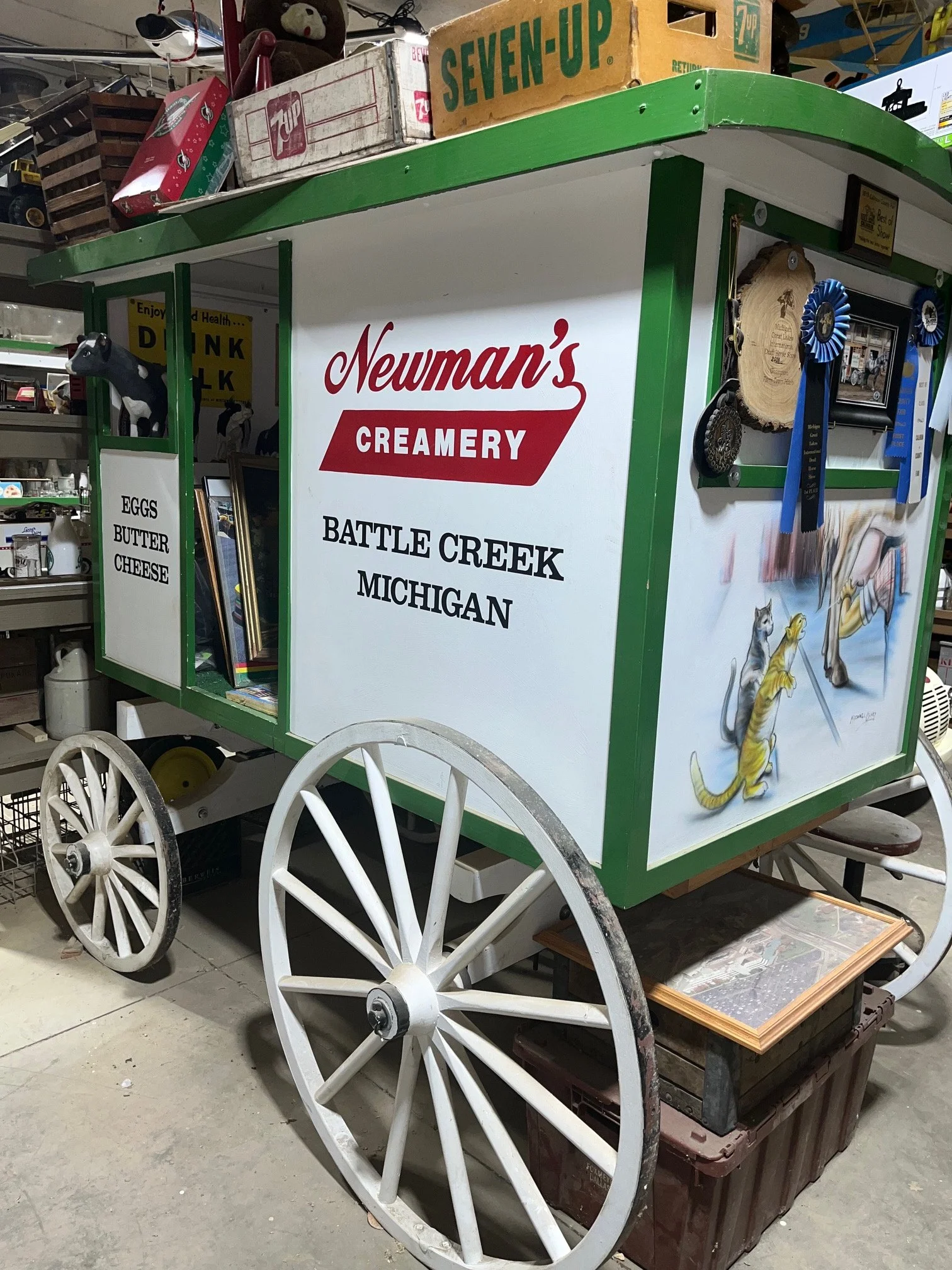 A white, old fashioned delivery wagon with wooden-spoke wheels, a green roof, and red lettering reading Newman's Creamery
