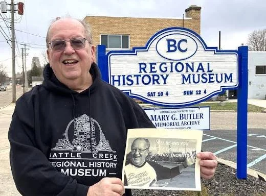 Kurt Thornton holds a picture of himself while standing in front of the museum building and sign