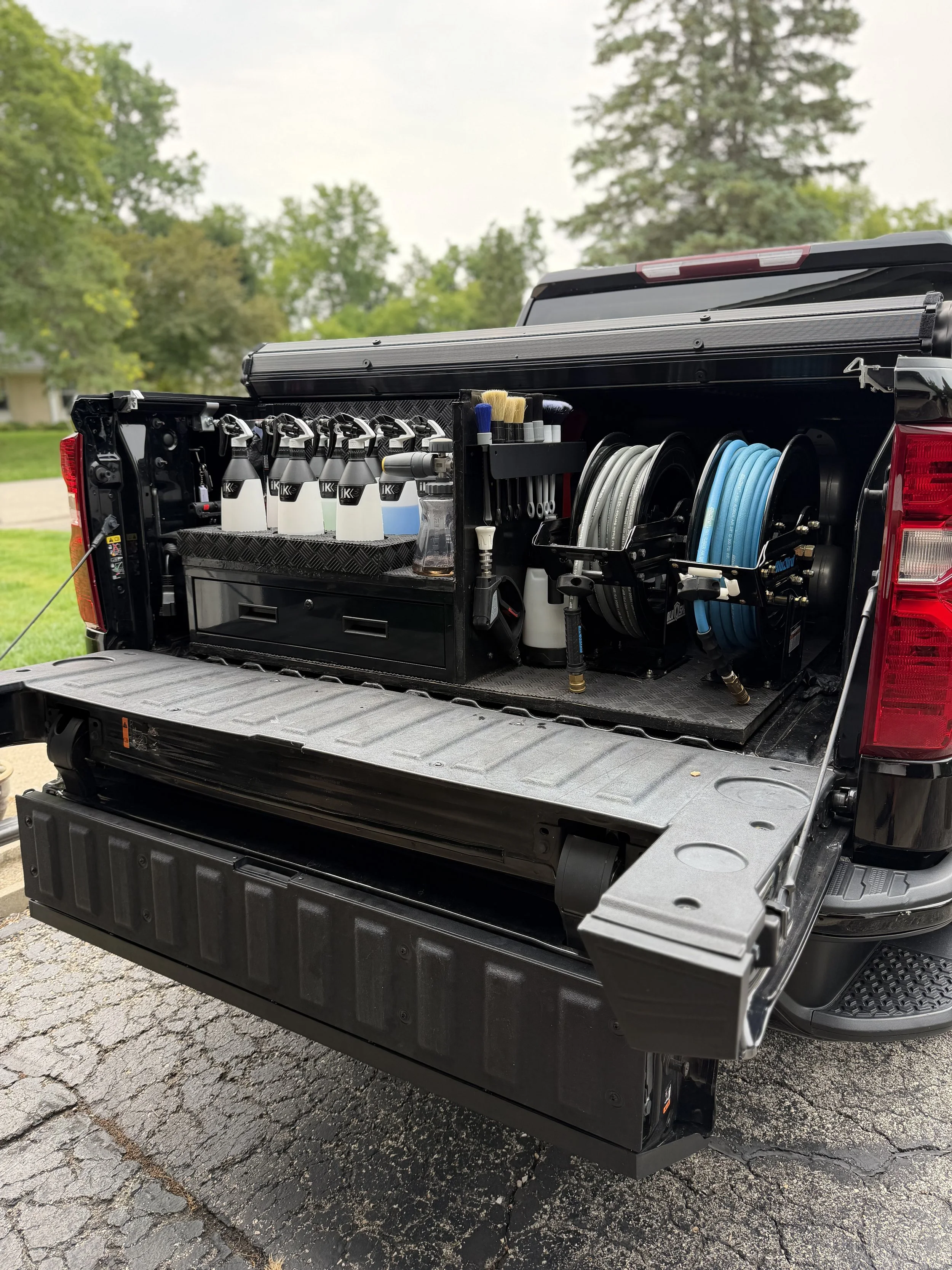 A truck equipped with a service bed containing cleaning supplies, hoses, brushes, and connectors, used for power washing or cleaning services.