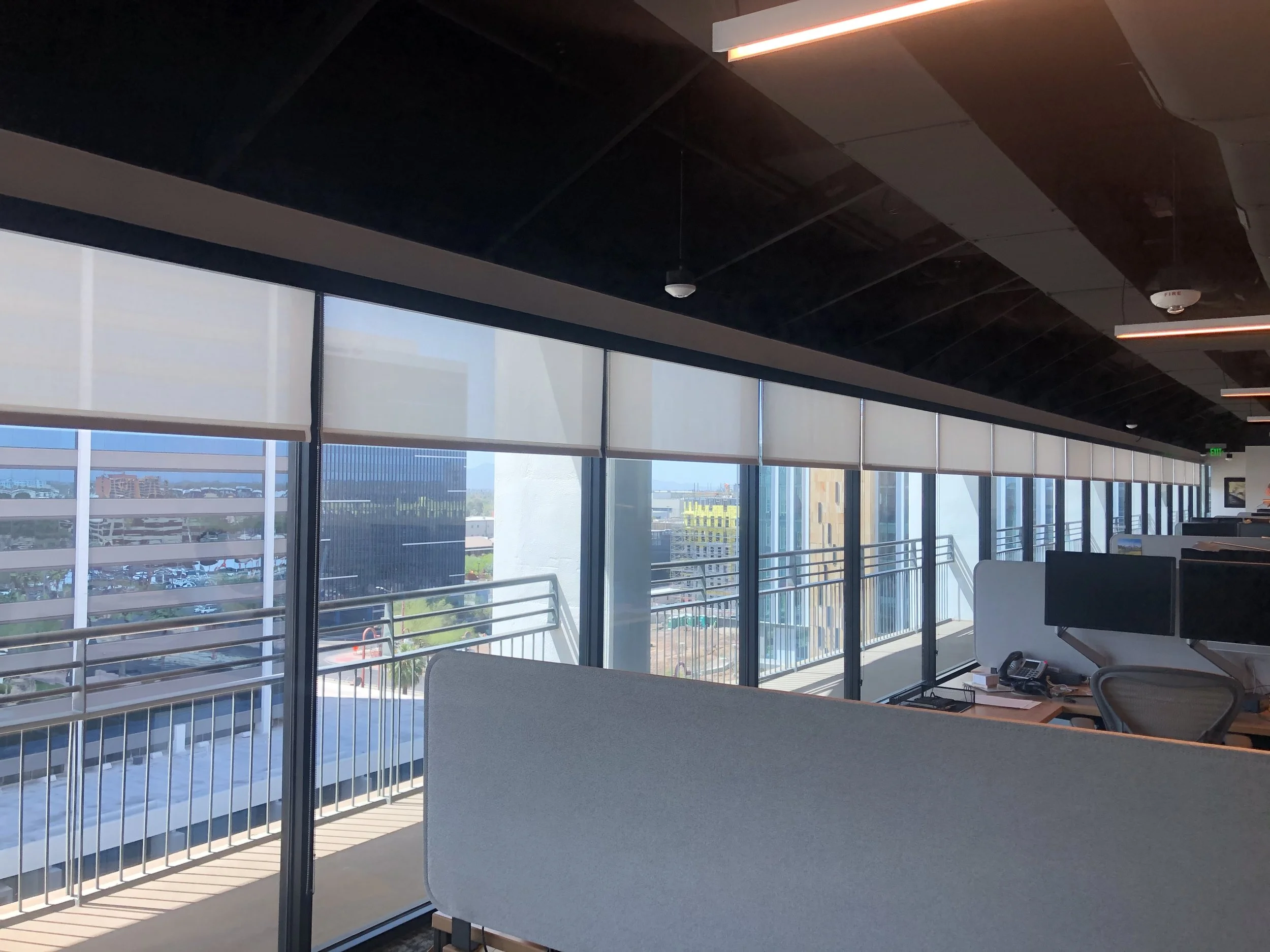 Interior of a modern office space with large windows, desks, chairs, and cityscape view outside.